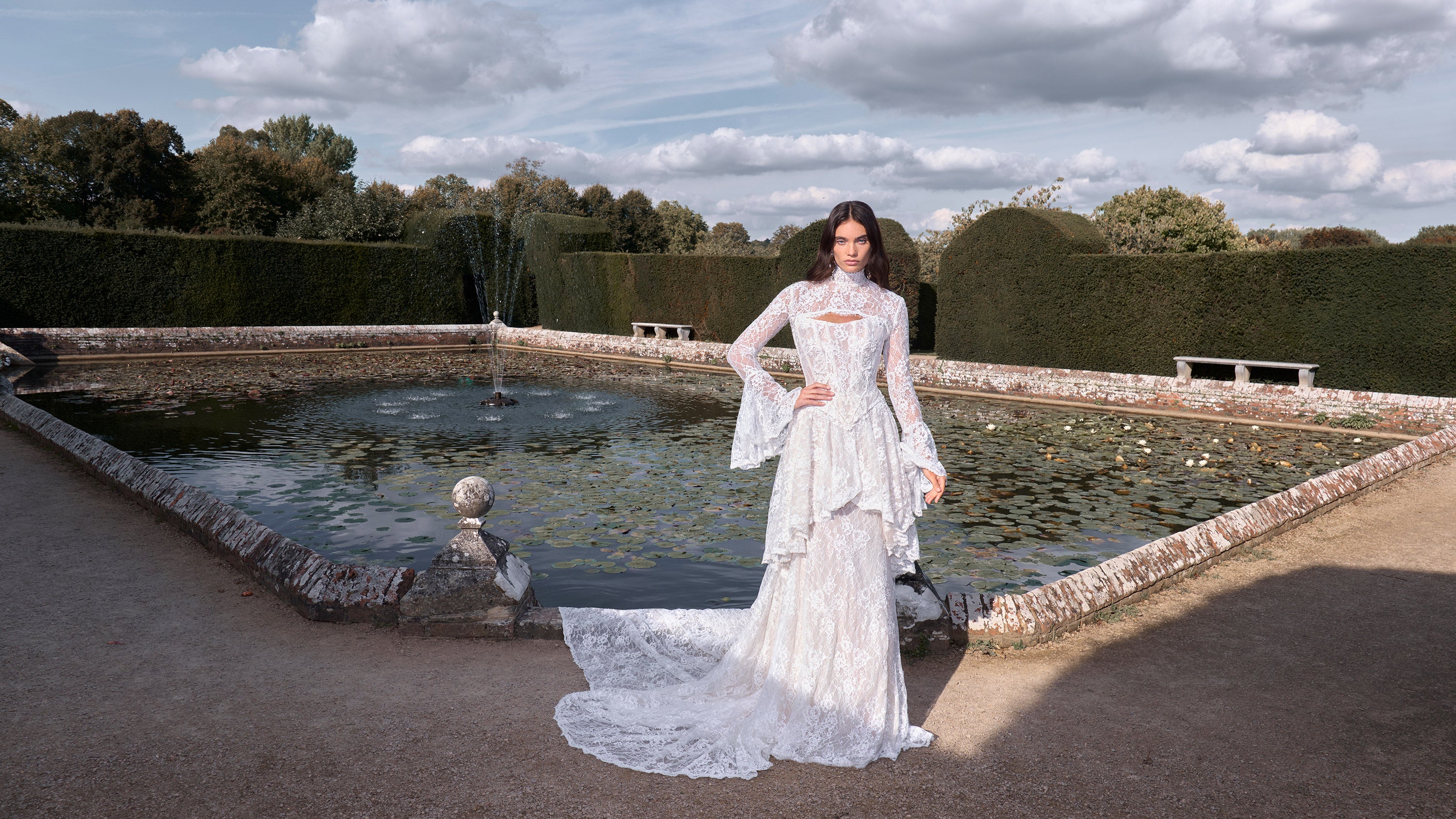 Woman in a white dress standing in a garden with a pond and trees in the background