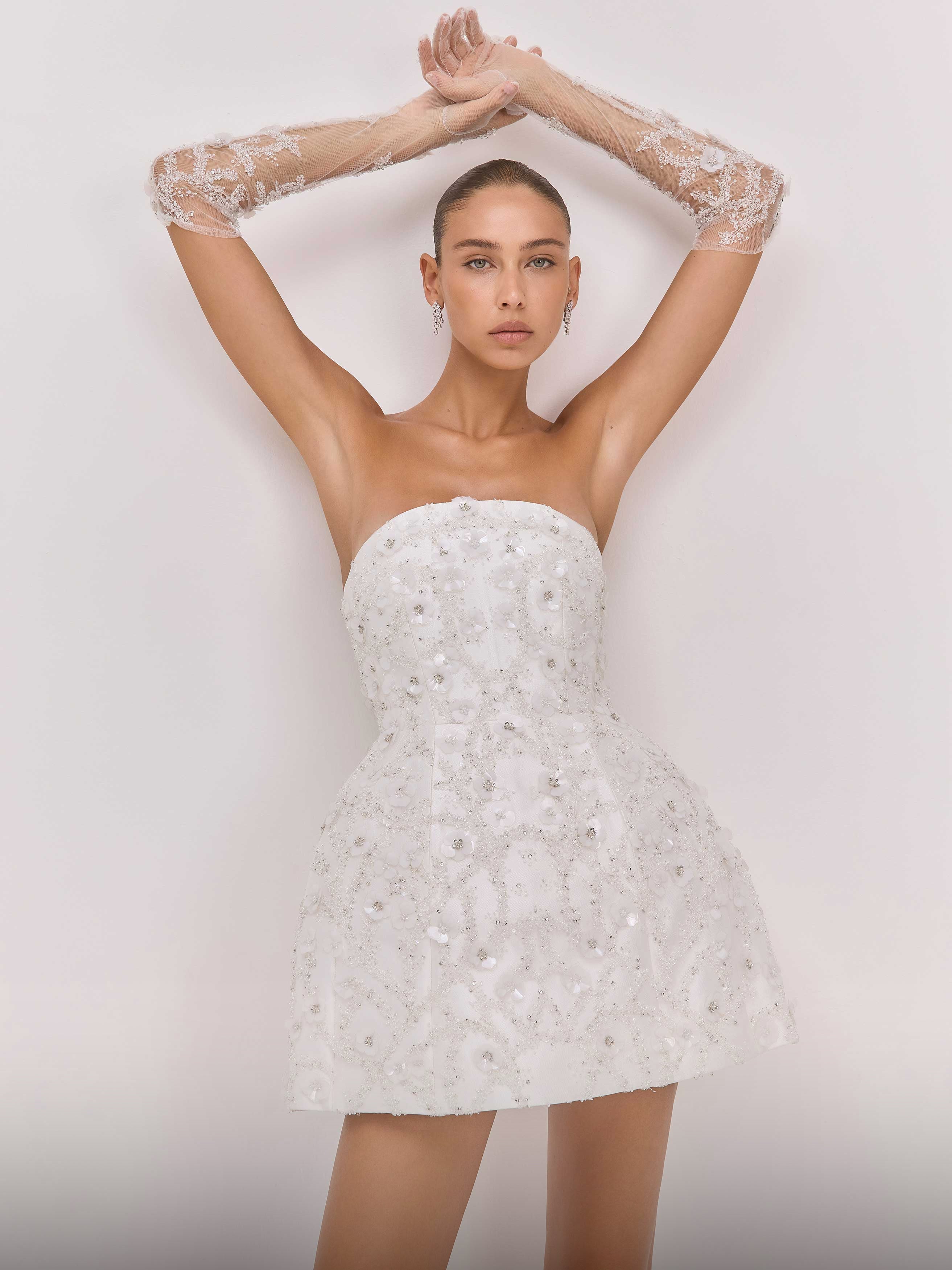 Woman wearing a white strapless dress with floral lace sleeves against a light background
