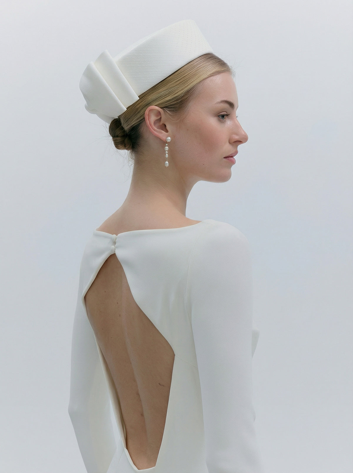 Woman wearing a white dress with a cutout back and a matching headpiece against a plain background