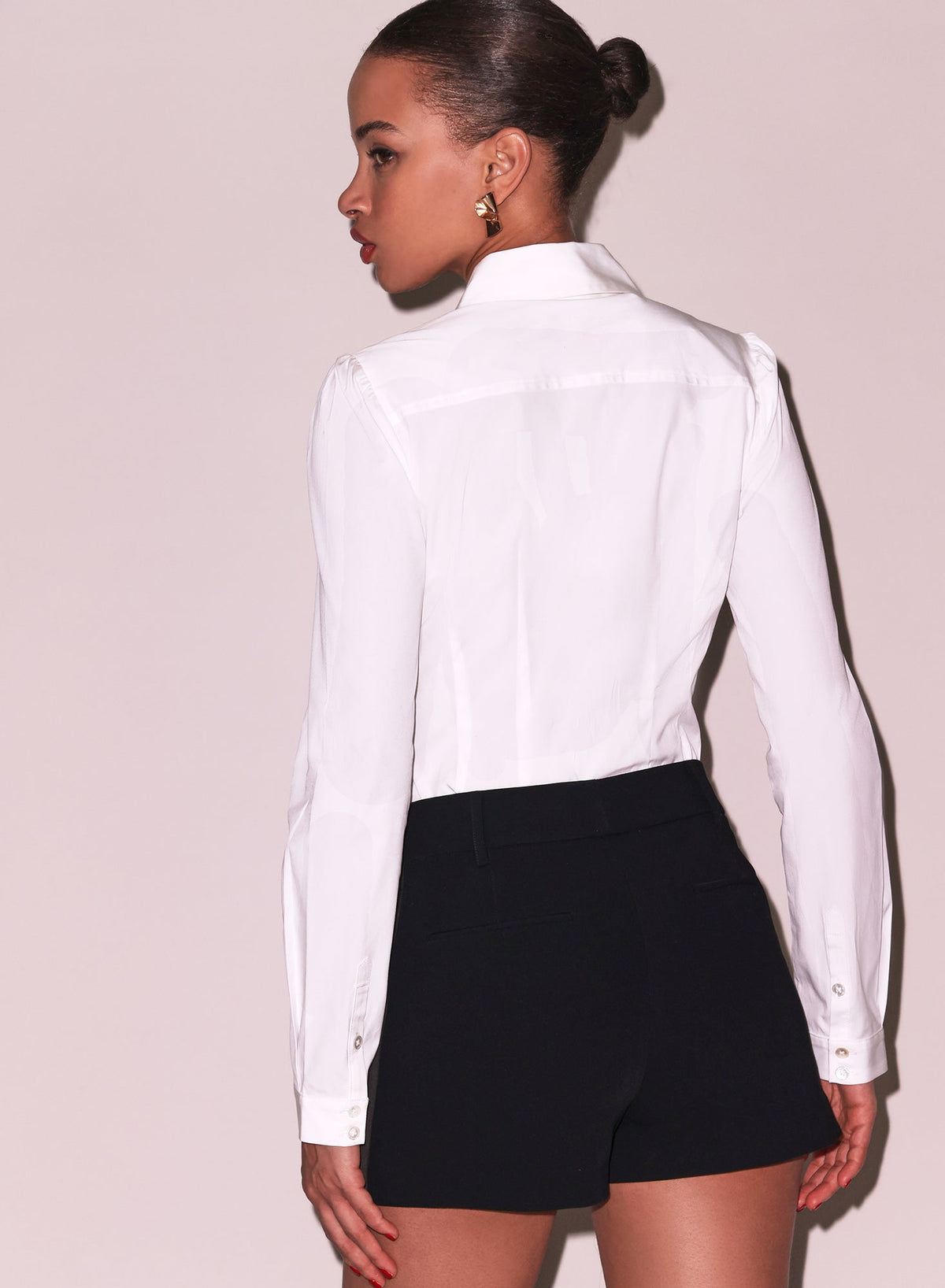 Person wearing a white blouse and black shorts against a plain background