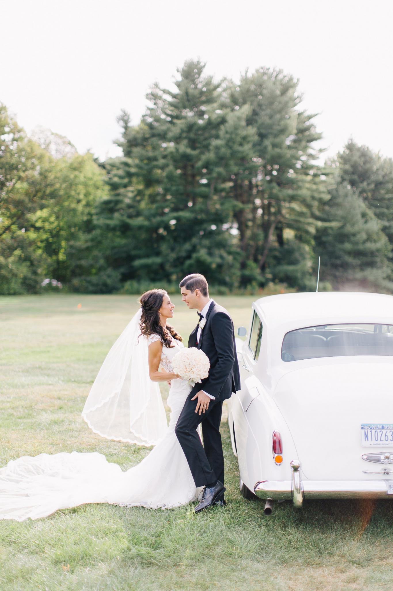 GL Bride Of the week Jennifer wearing the Fiona next to a vintage car looking at her groom
