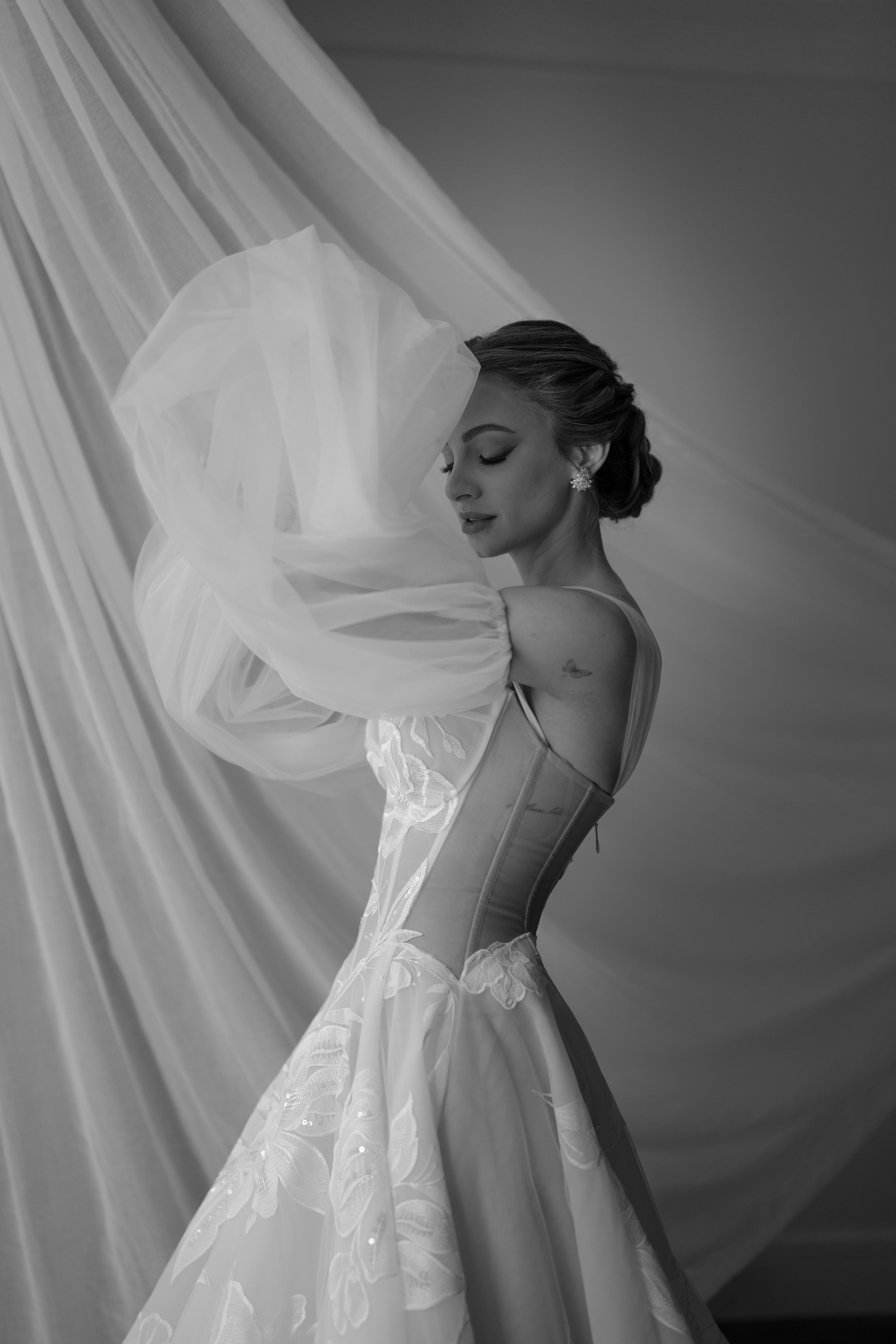 Black and white photo of GL Bride Carina wearing the Evelyn wedding gown, with a flowing veil.