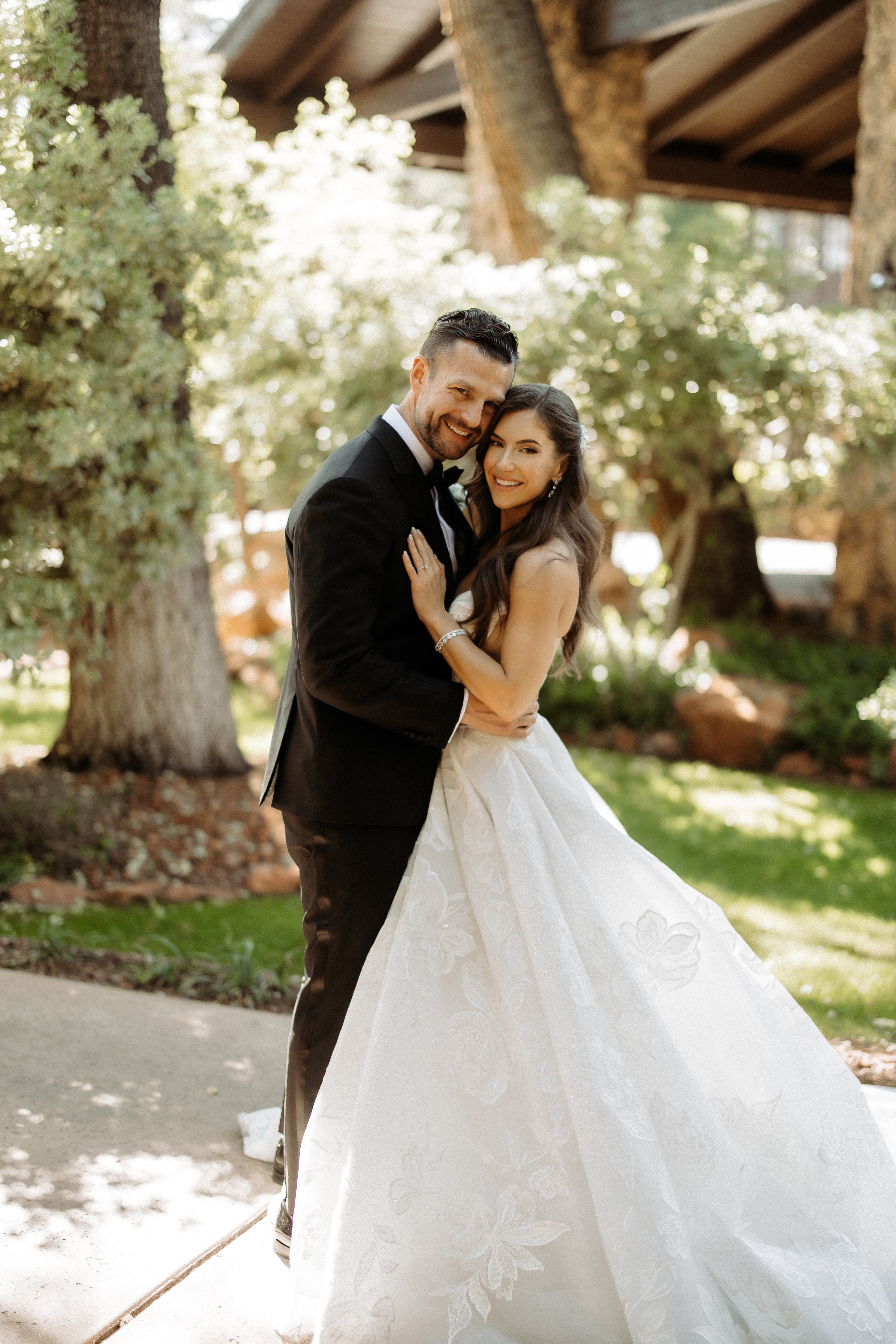 Man in a suit and woman in our Evelyn dress standing together outdoors with trees in the background