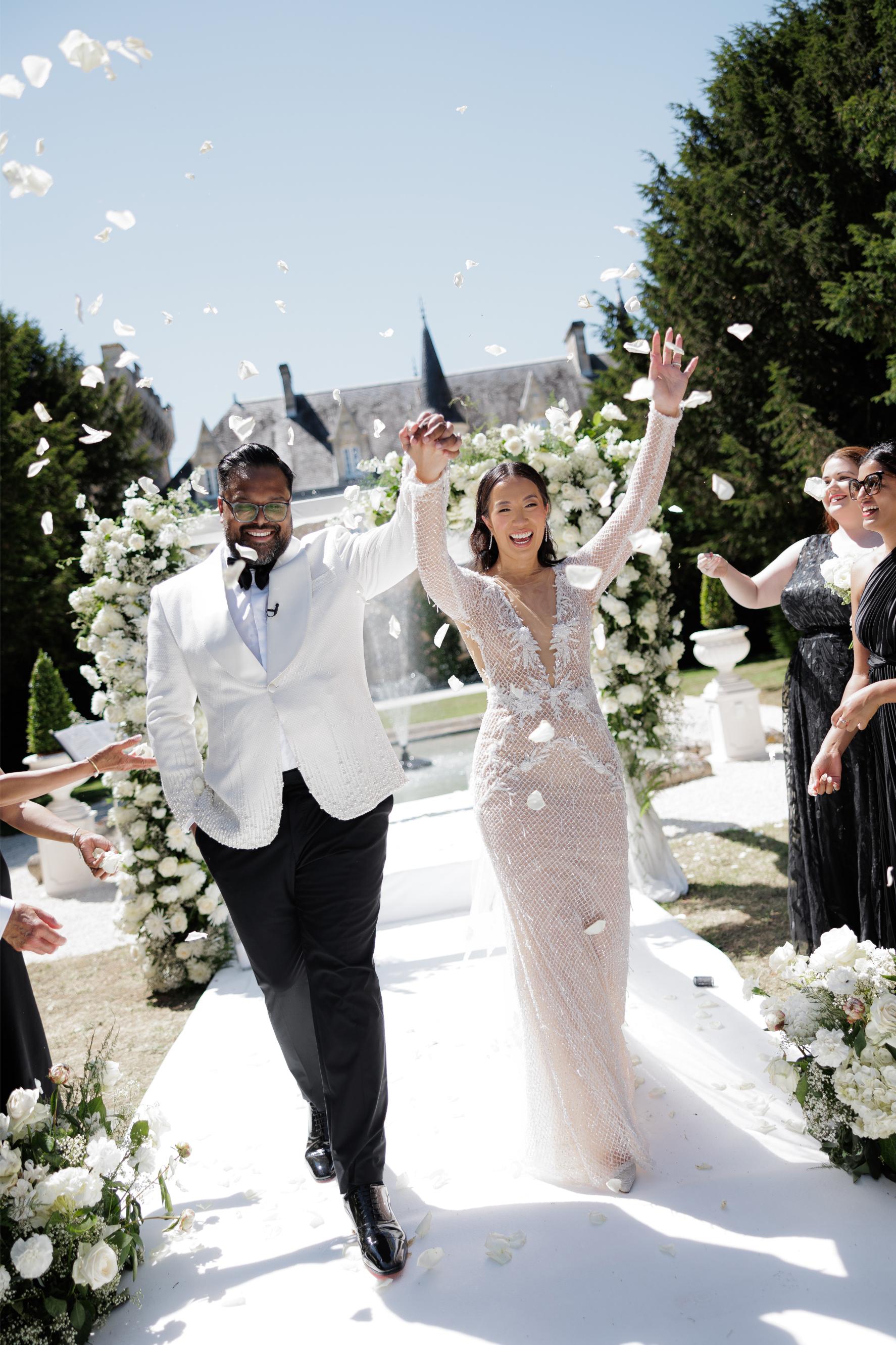 Wedding couple walking down an aisle with confetti falling around them, surrounded by floral decorations and guests.