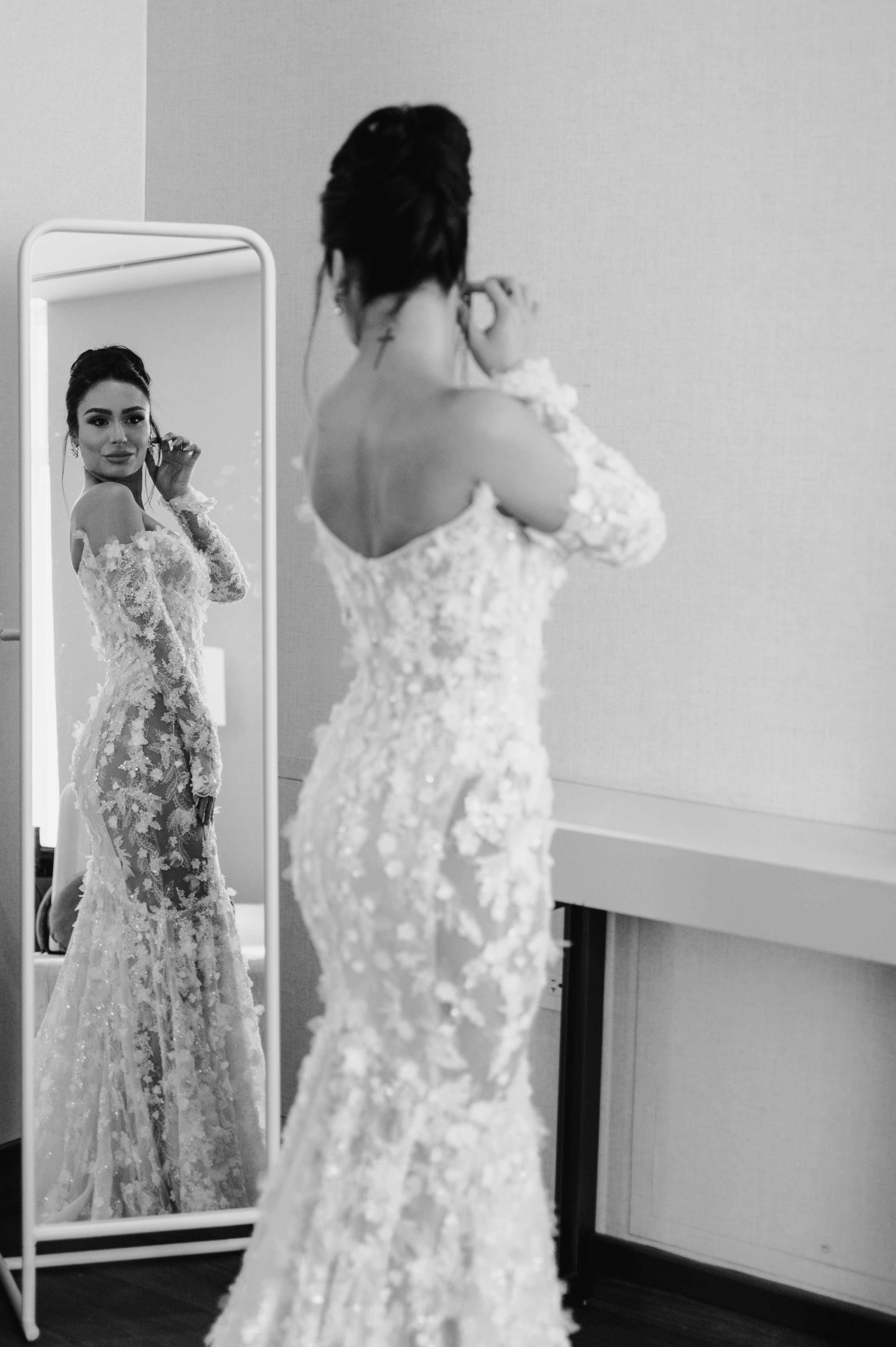 GL Bride Eva in our Maya standing in front of a mirror, adjusting her hair.