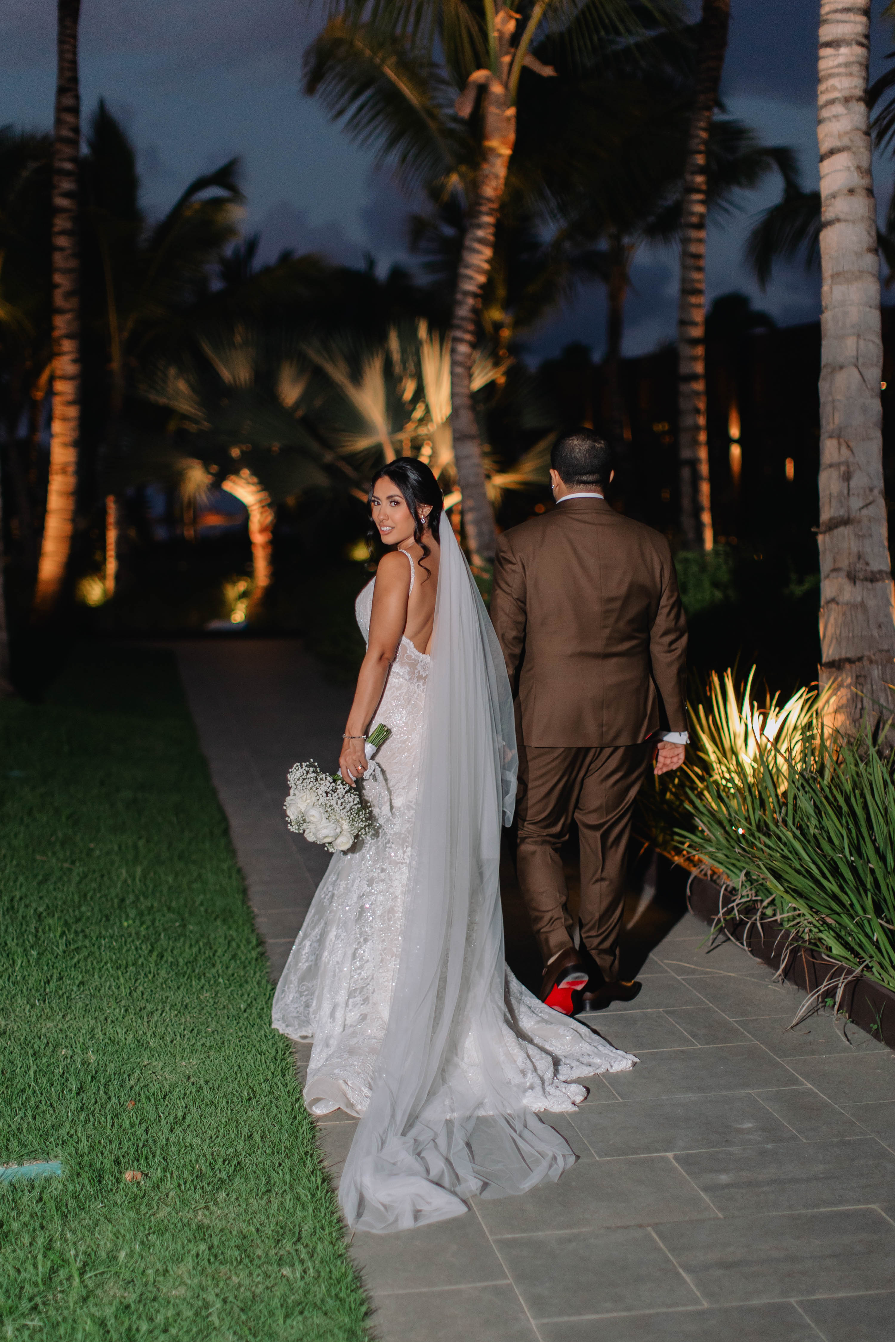 Bride and groom walking together at night with palm trees in the background