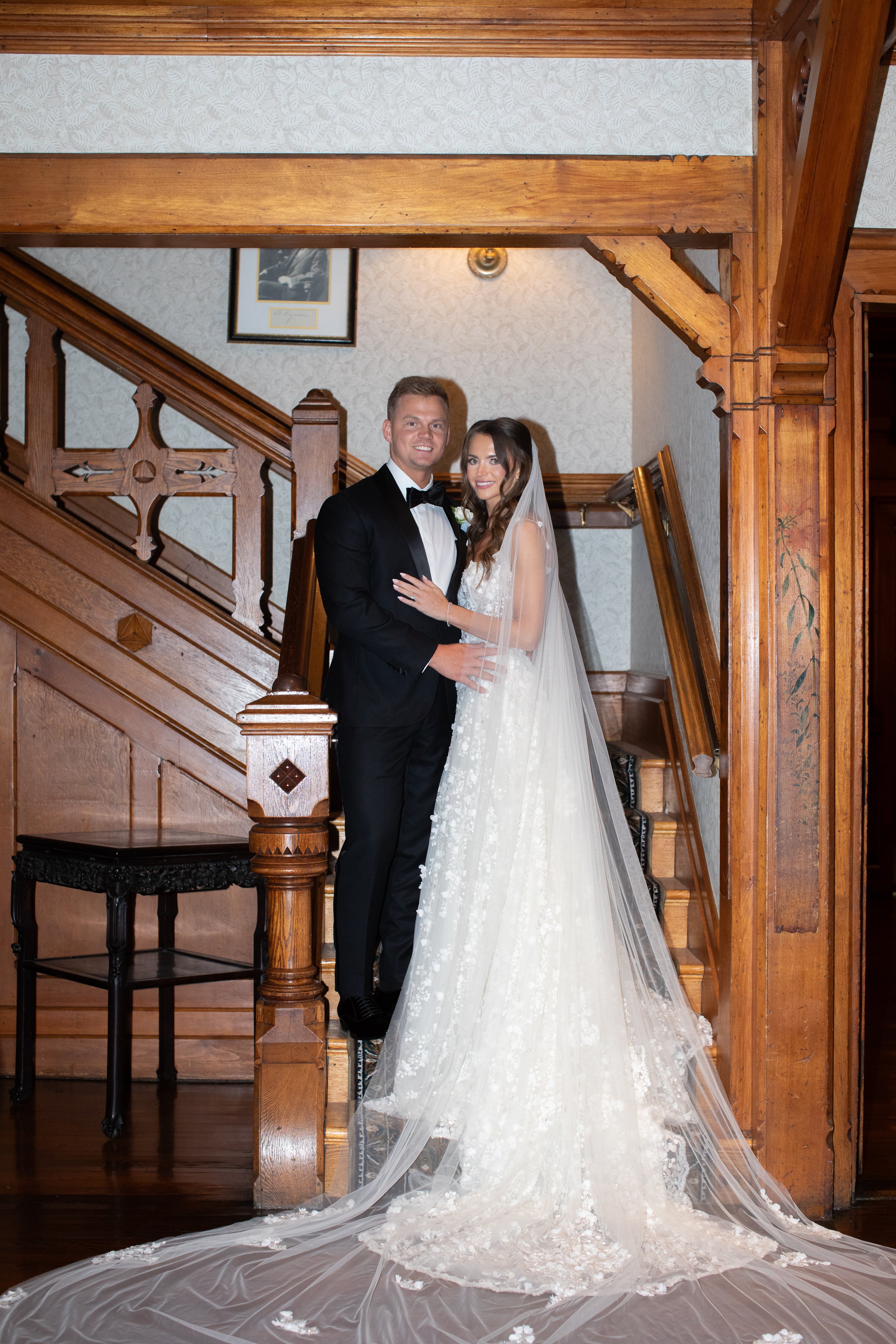 Man and woman in formal attire standing in a staircase with wooden railings.