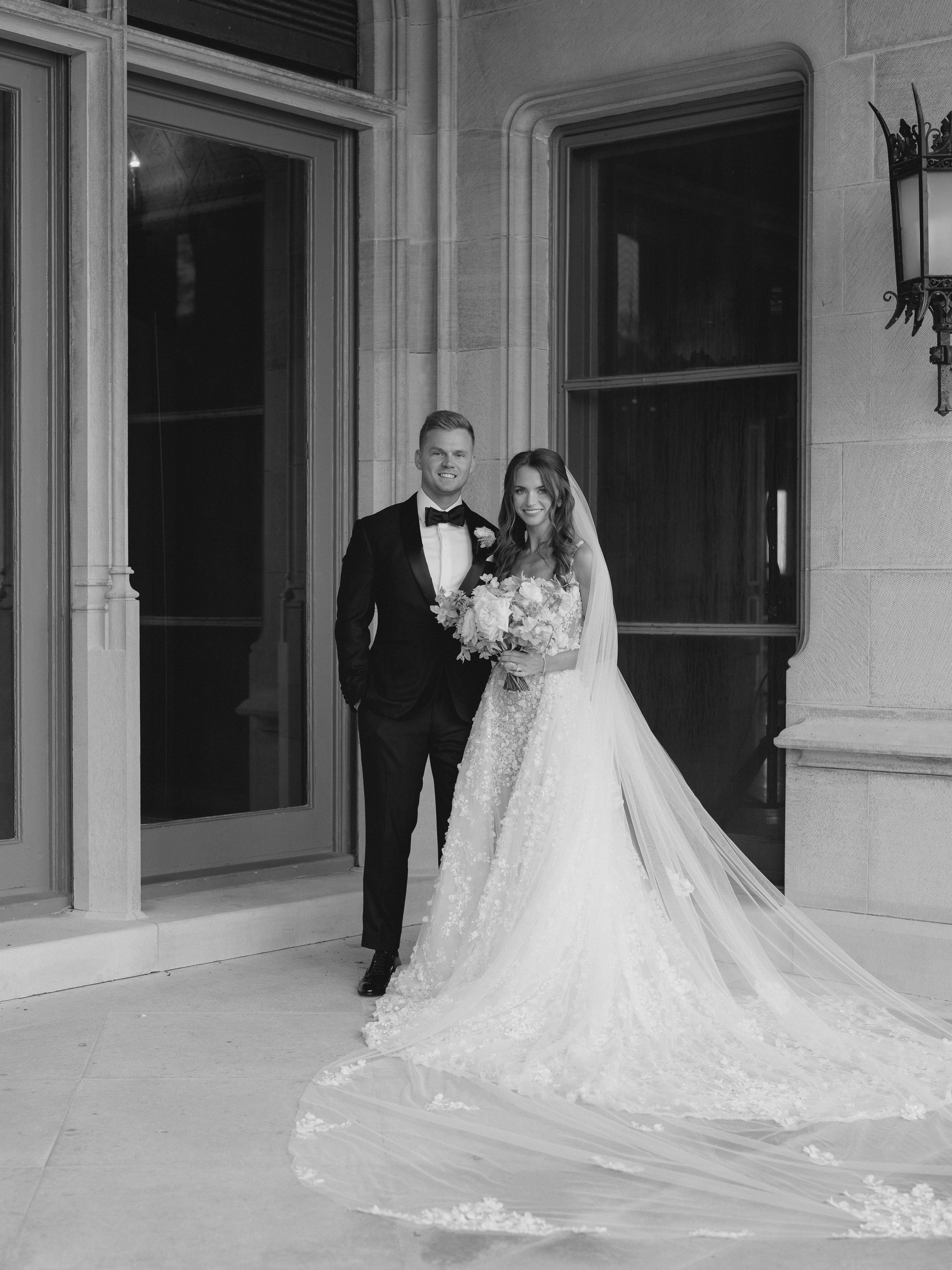 Black and white photo of a bride and groom standing in front of a large door.