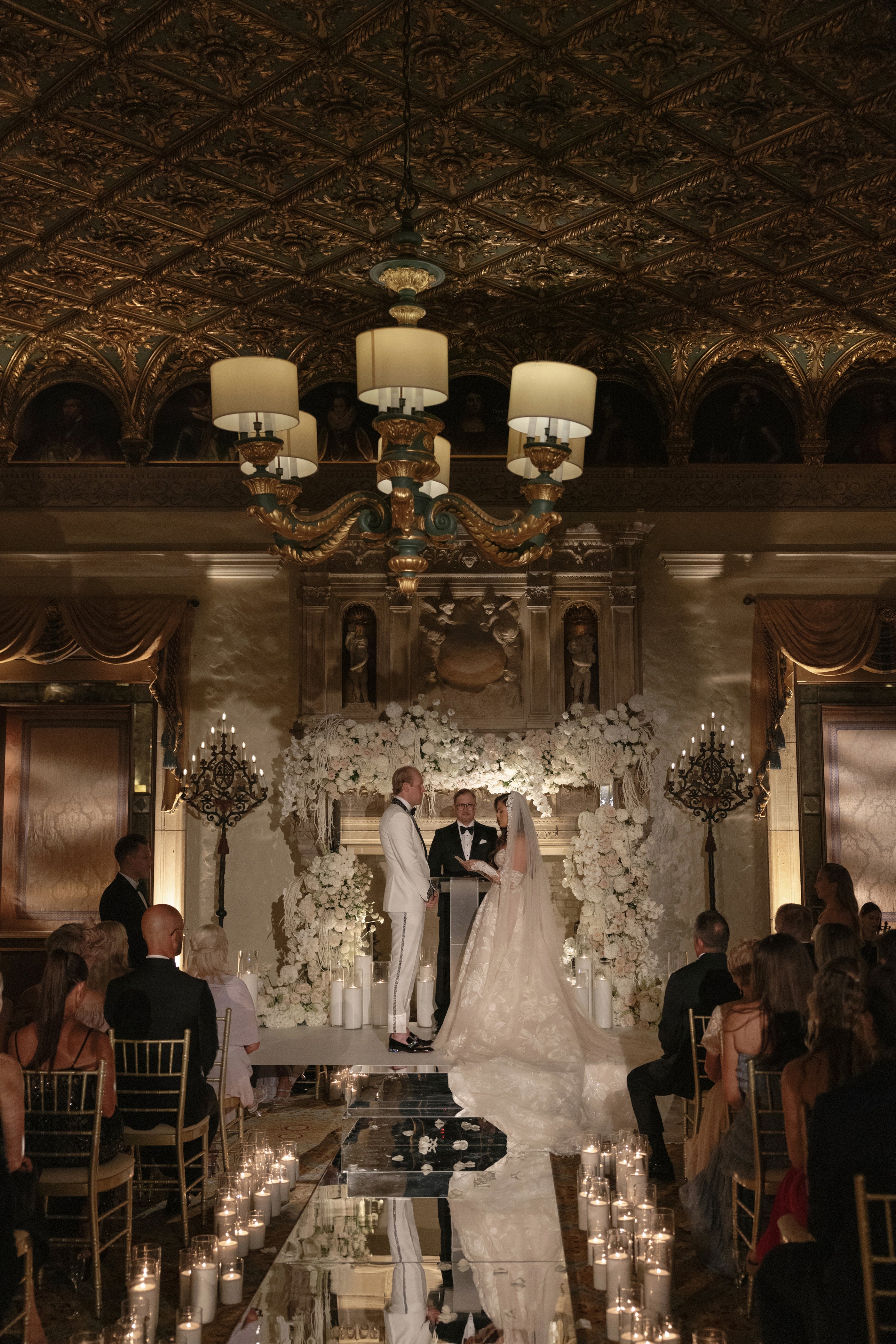 Wedding ceremony taking place in an elegant indoor setting with chandeliers and decorative elements.
