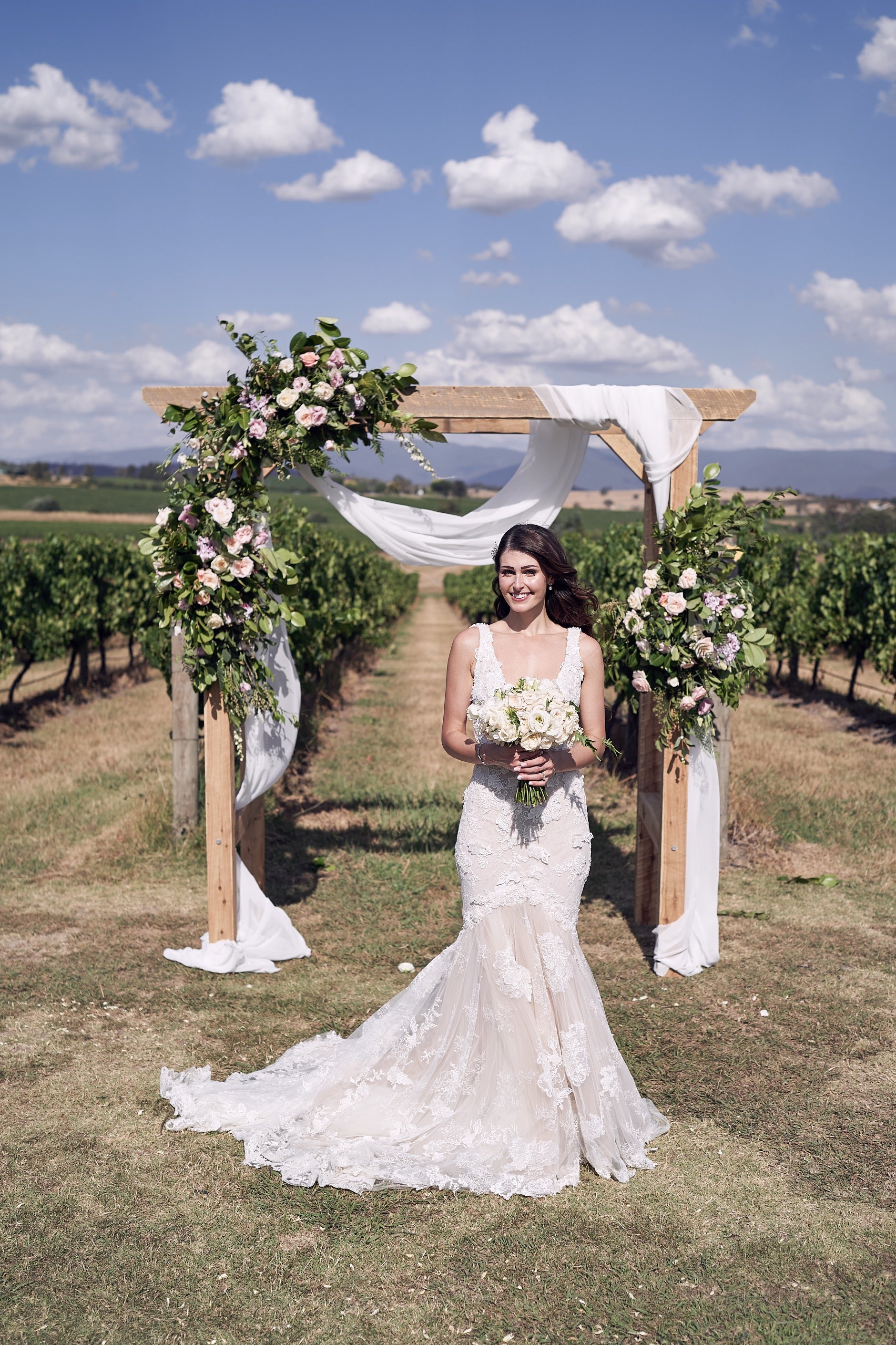 GL Bride Nadia in front of the wedding arch in a vineyard