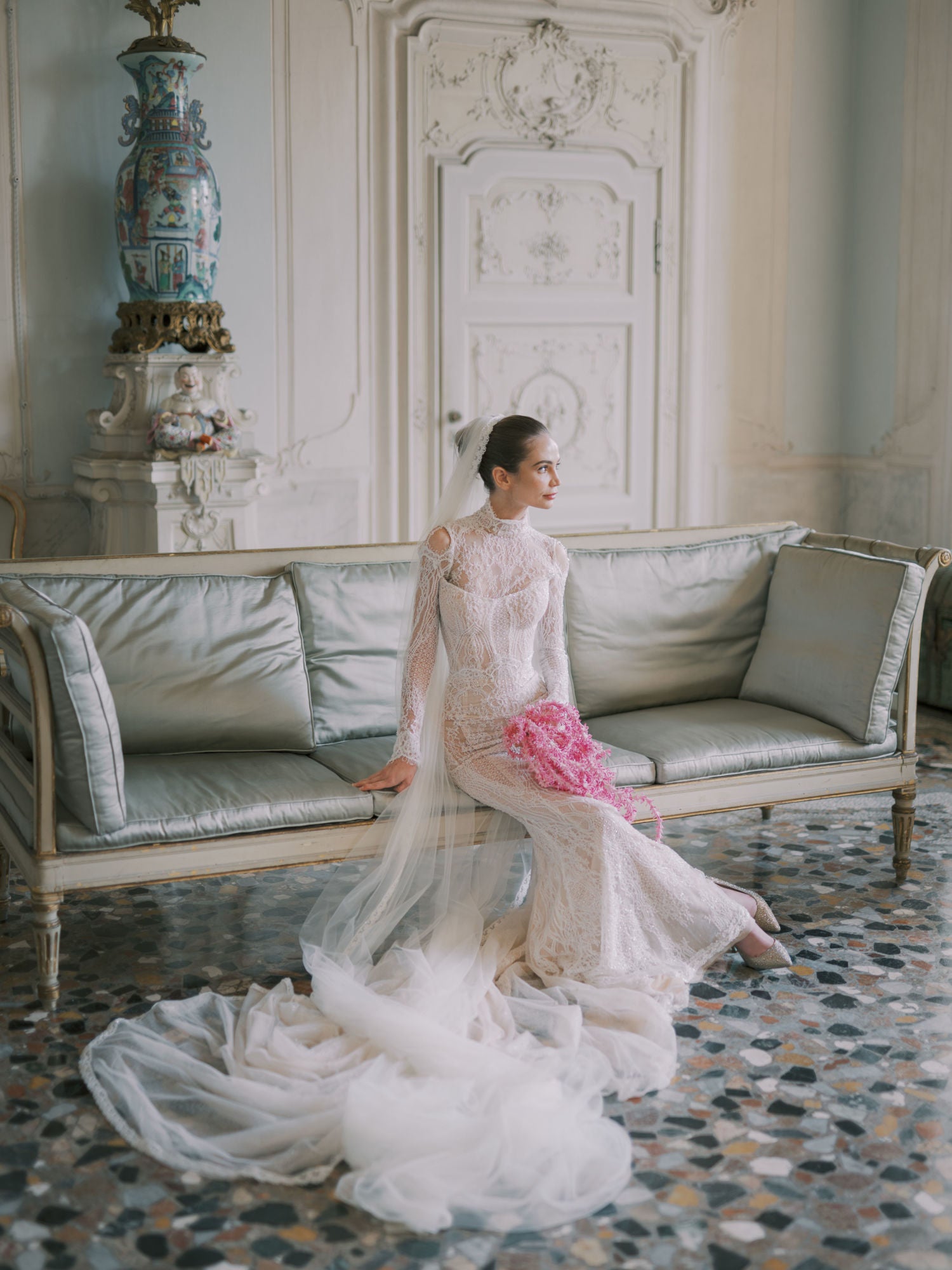 GL Bride Sarah in our Élysée gown with a long train sitting on a decorative couch in an elegant room.
