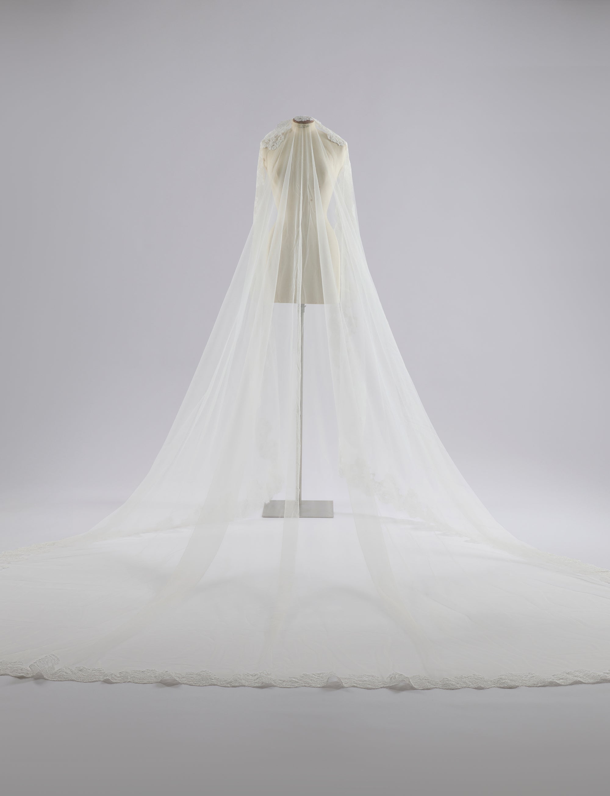 Woman in a white lace wedding dress standing in an elegant room with red curtains and chandelier.