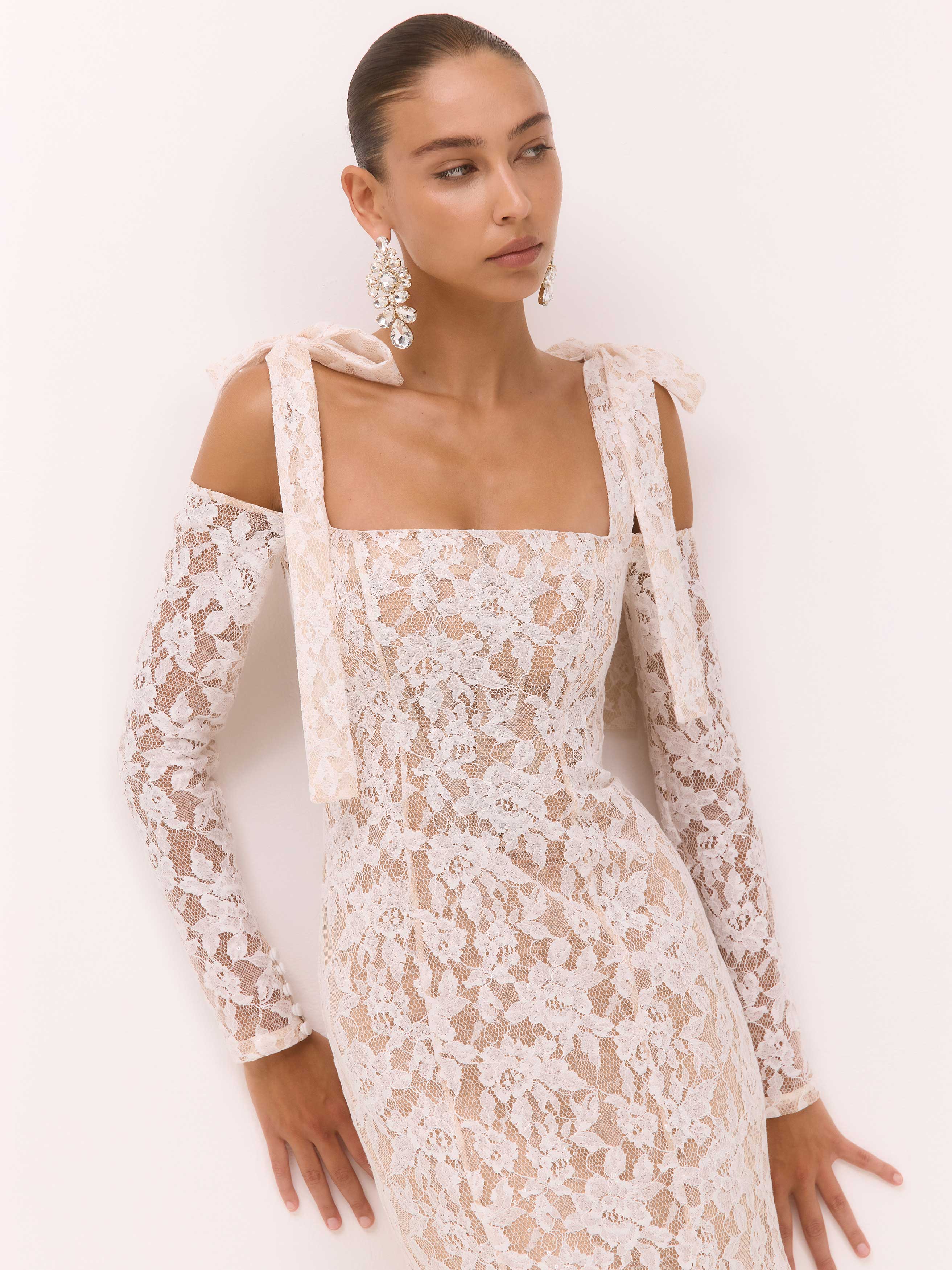 Woman wearing a white lace dress with long sleeves on a plain background