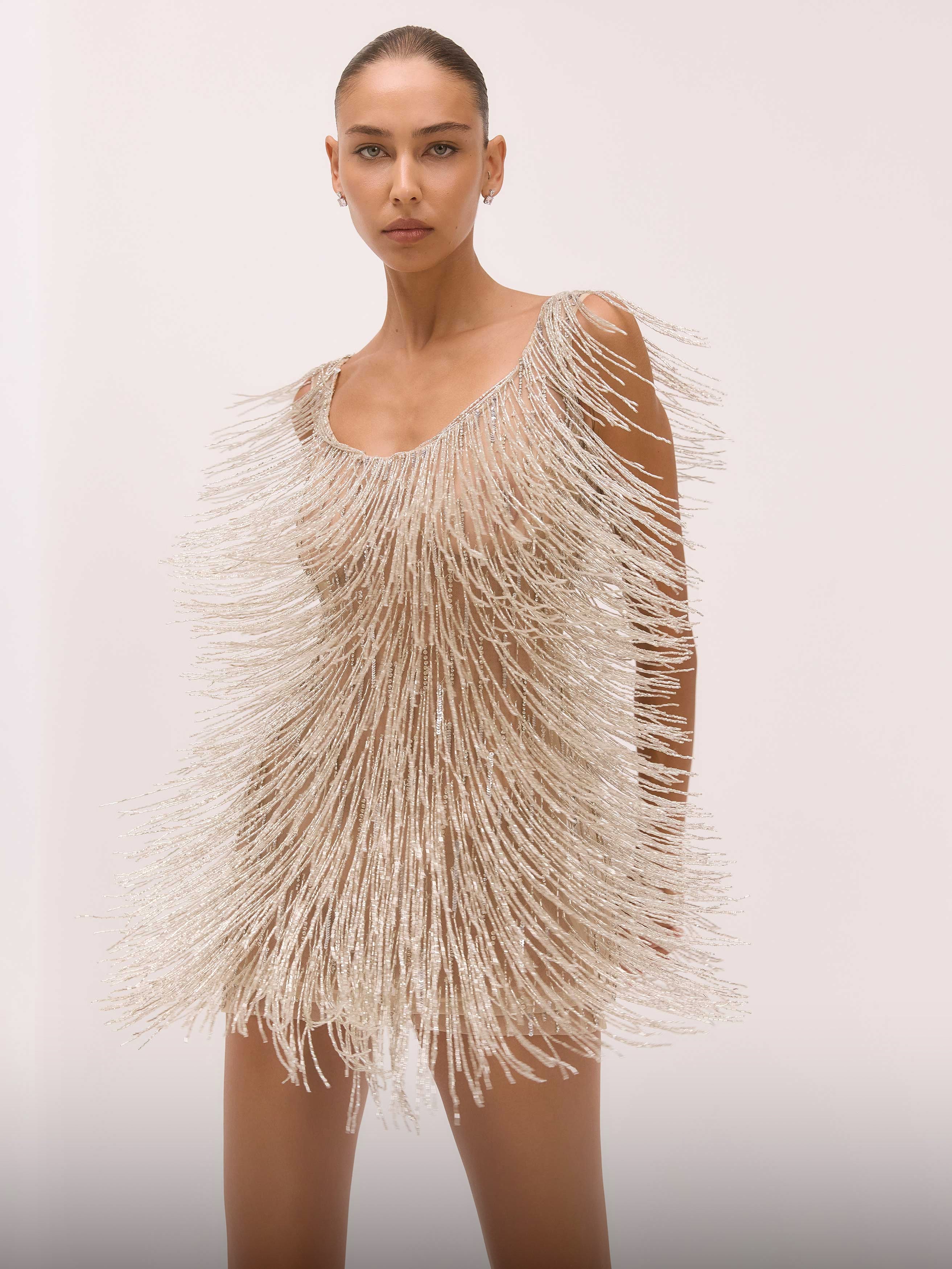 Model wearing a beige fringe dress against a plain background