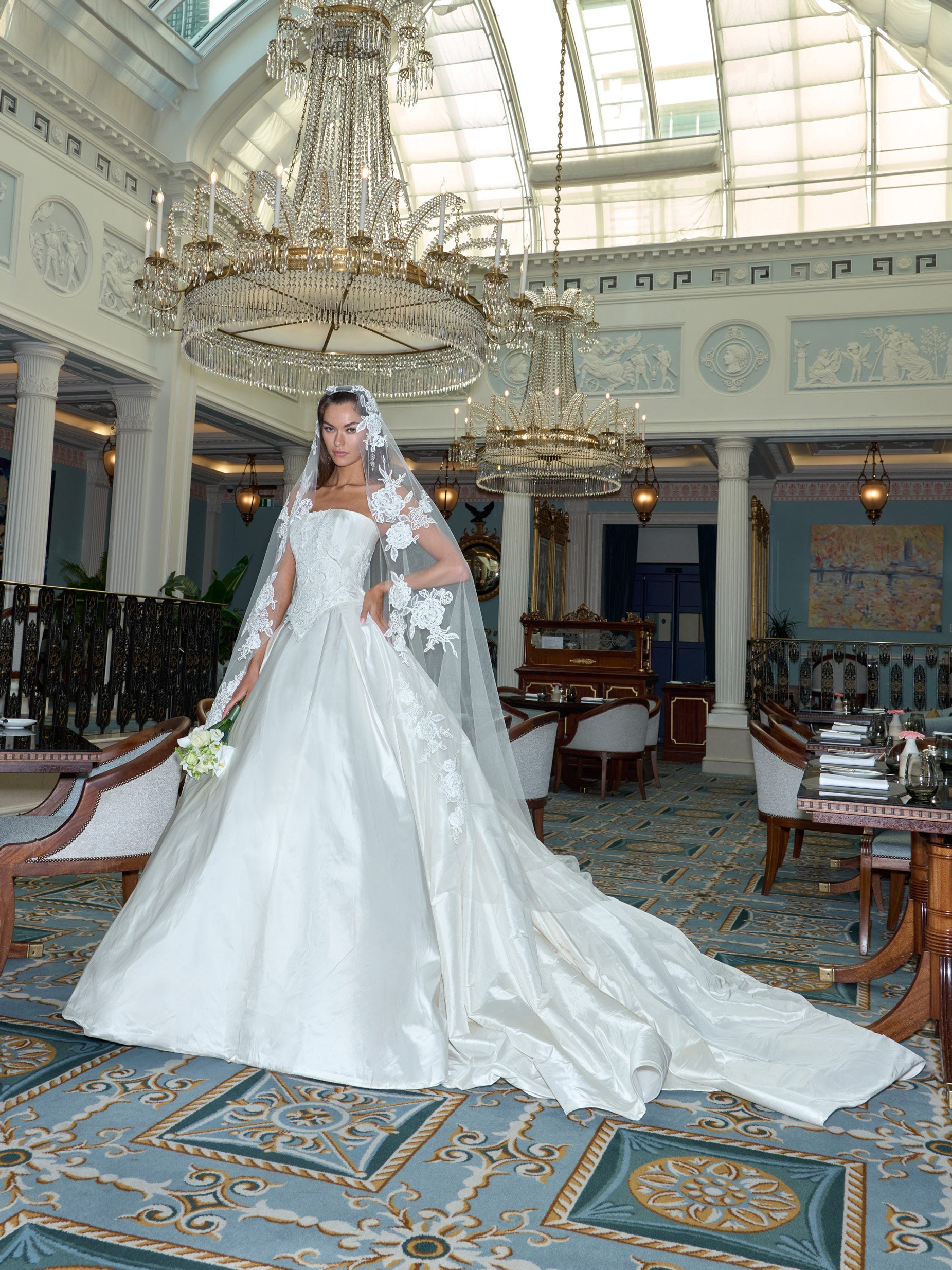 Woman in a white wedding dress standing in an elegant indoor setting with chandeliers.
