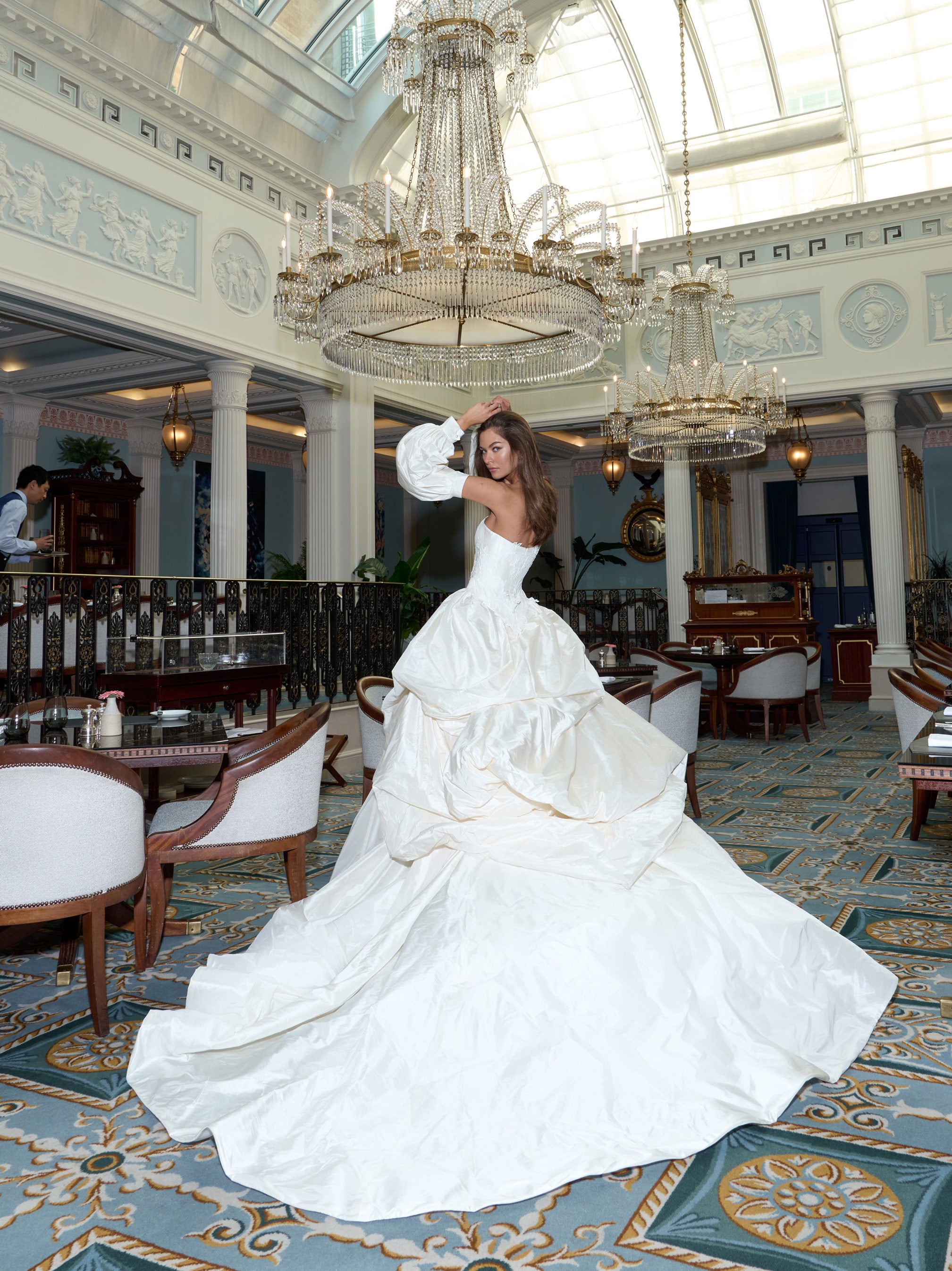 Woman in a white wedding dress standing in an elegant indoor setting with chandeliers.