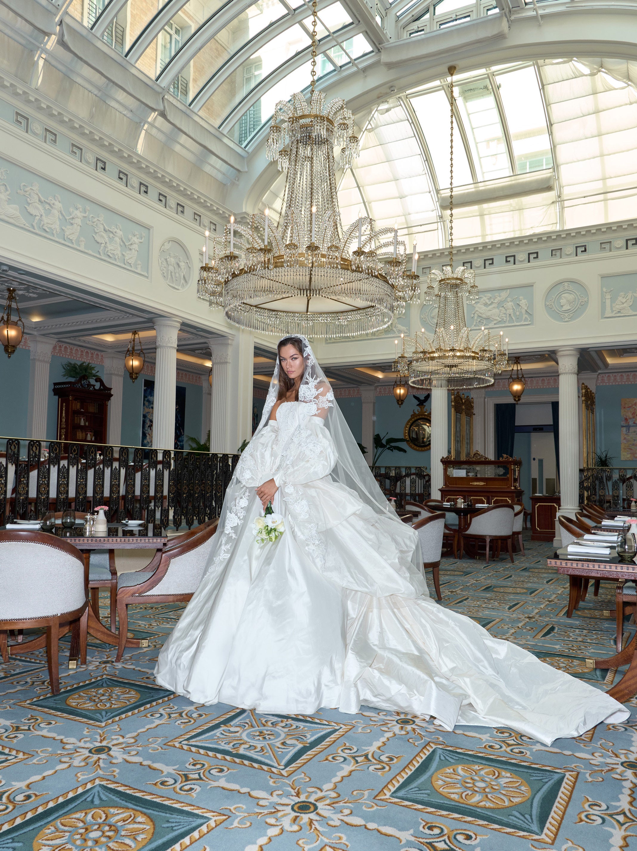 Woman in a white wedding dress standing in an elegant indoor setting with chandeliers.