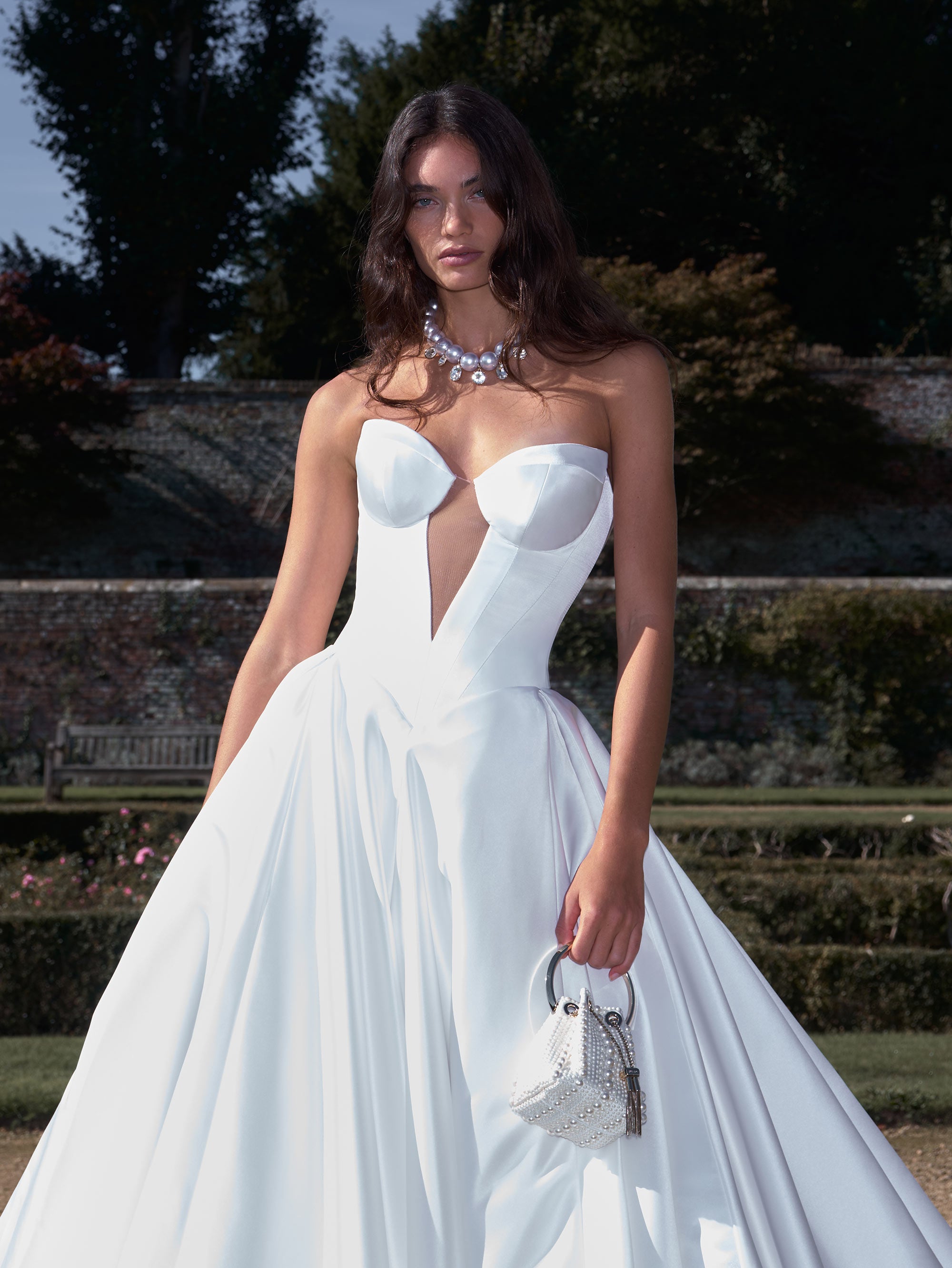 Woman in a white wedding dress standing outdoors with greenery in the background