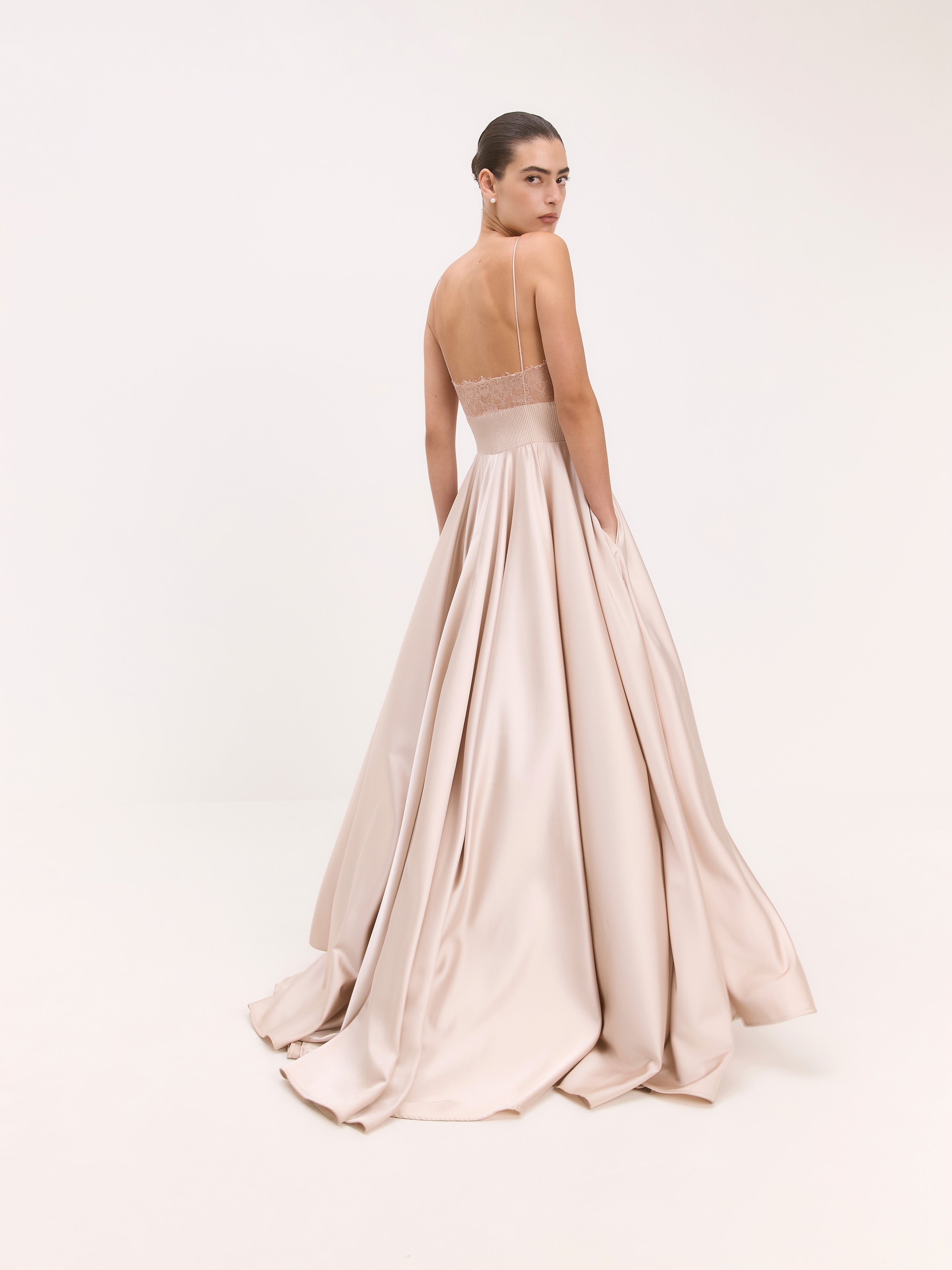 Woman wearing a blush pink gown with a sheer back on a white background