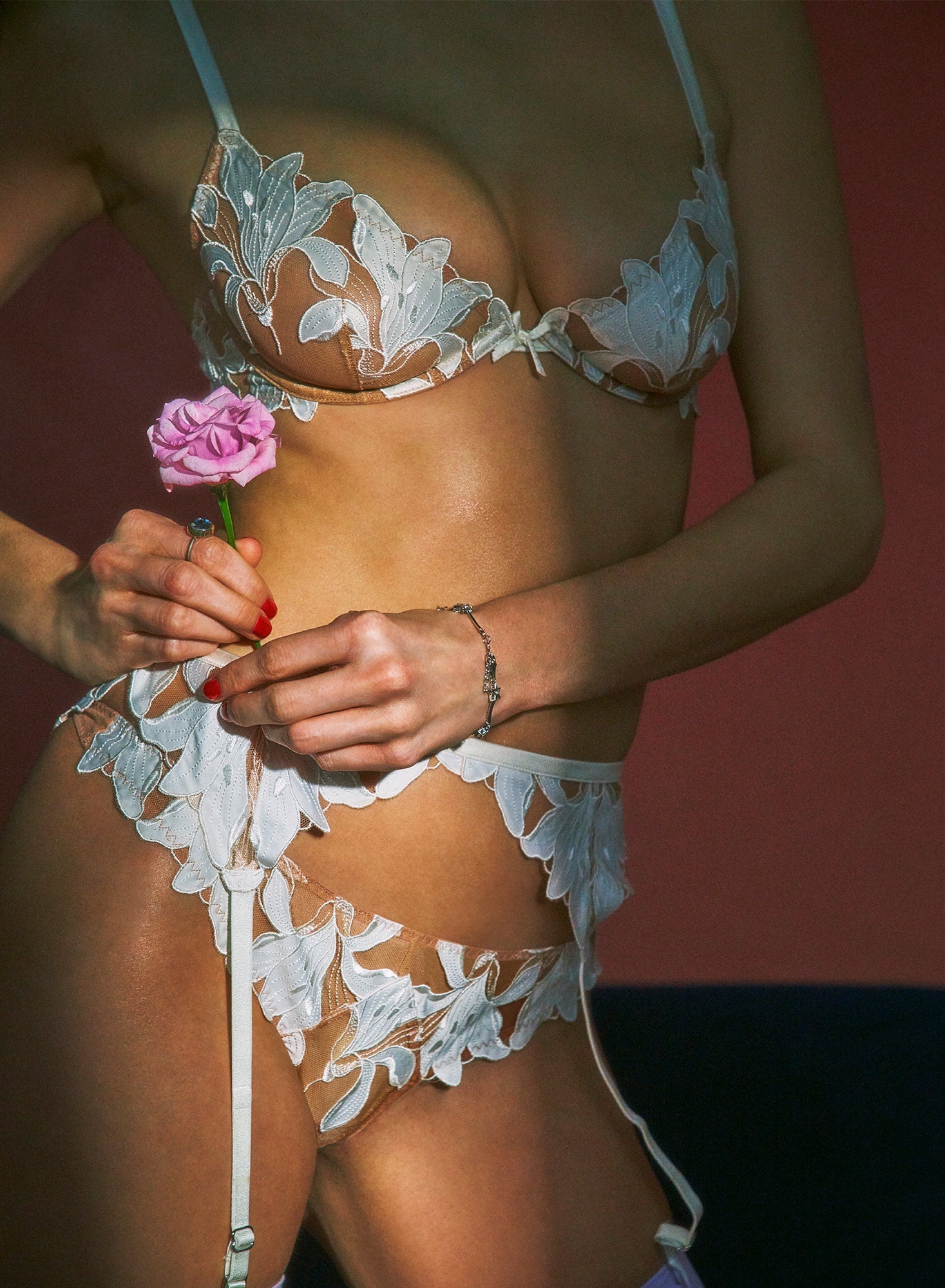 Person wearing white lace lingerie holding a pink flower against a blurred background