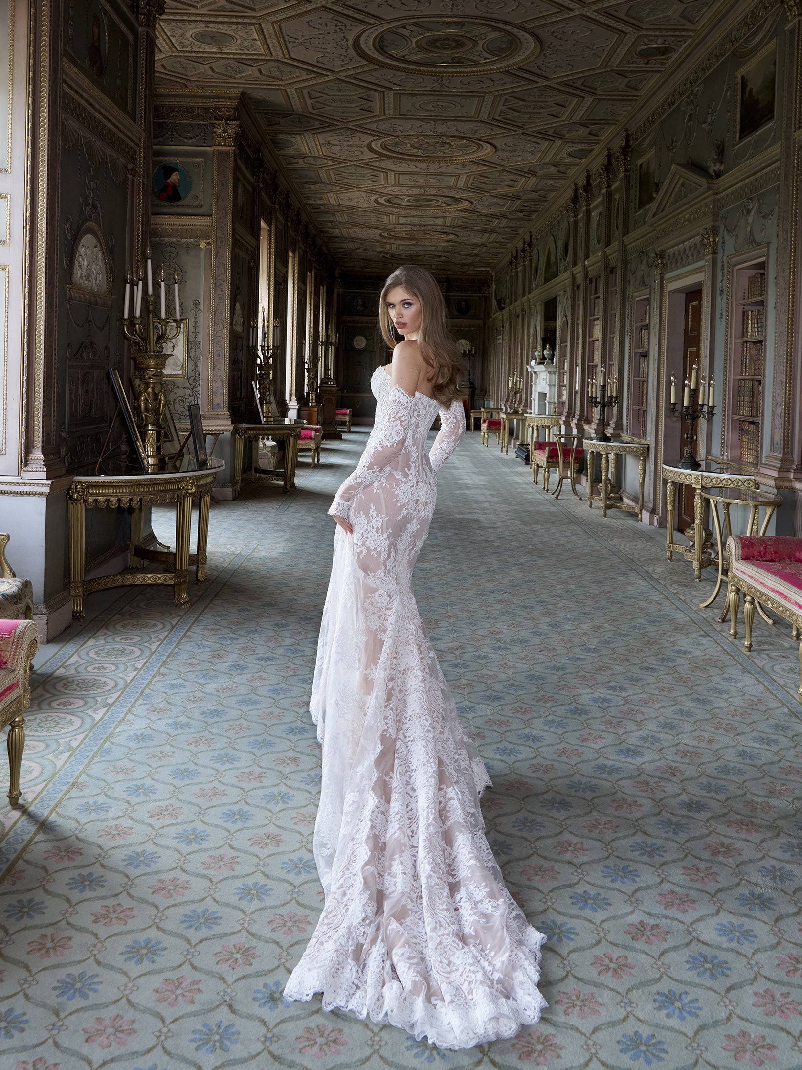 Woman in a white lace gown standing in an ornate hallway