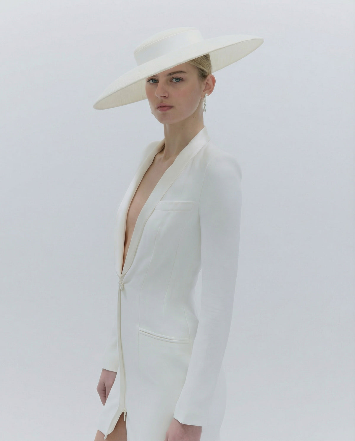 Woman wearing a white outfit with a wide-brimmed hat on a plain background