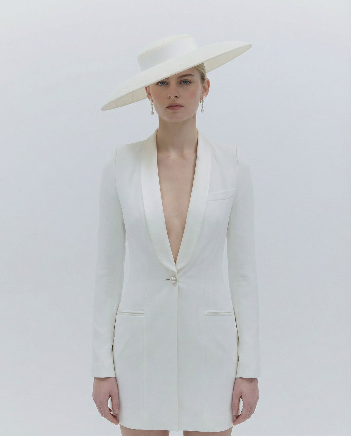 Woman wearing a white blazer dress and hat on a light gray background