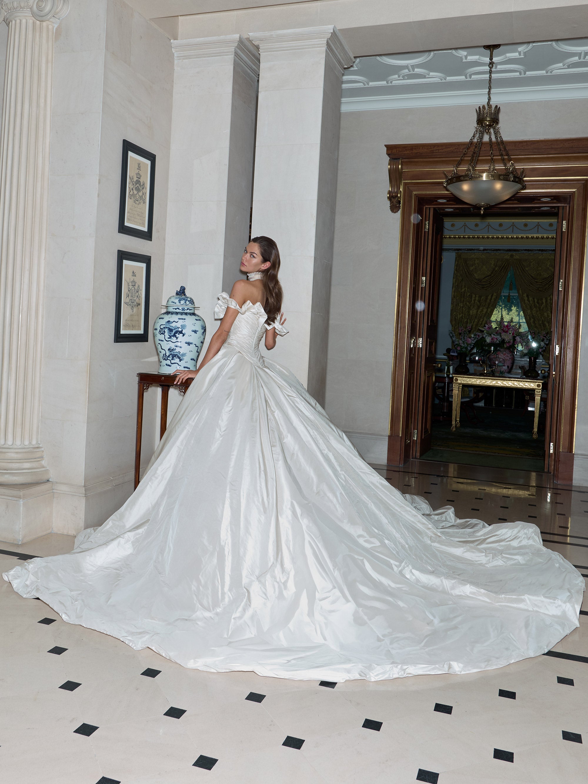 Woman in a white wedding dress standing in an elegant interior setting.