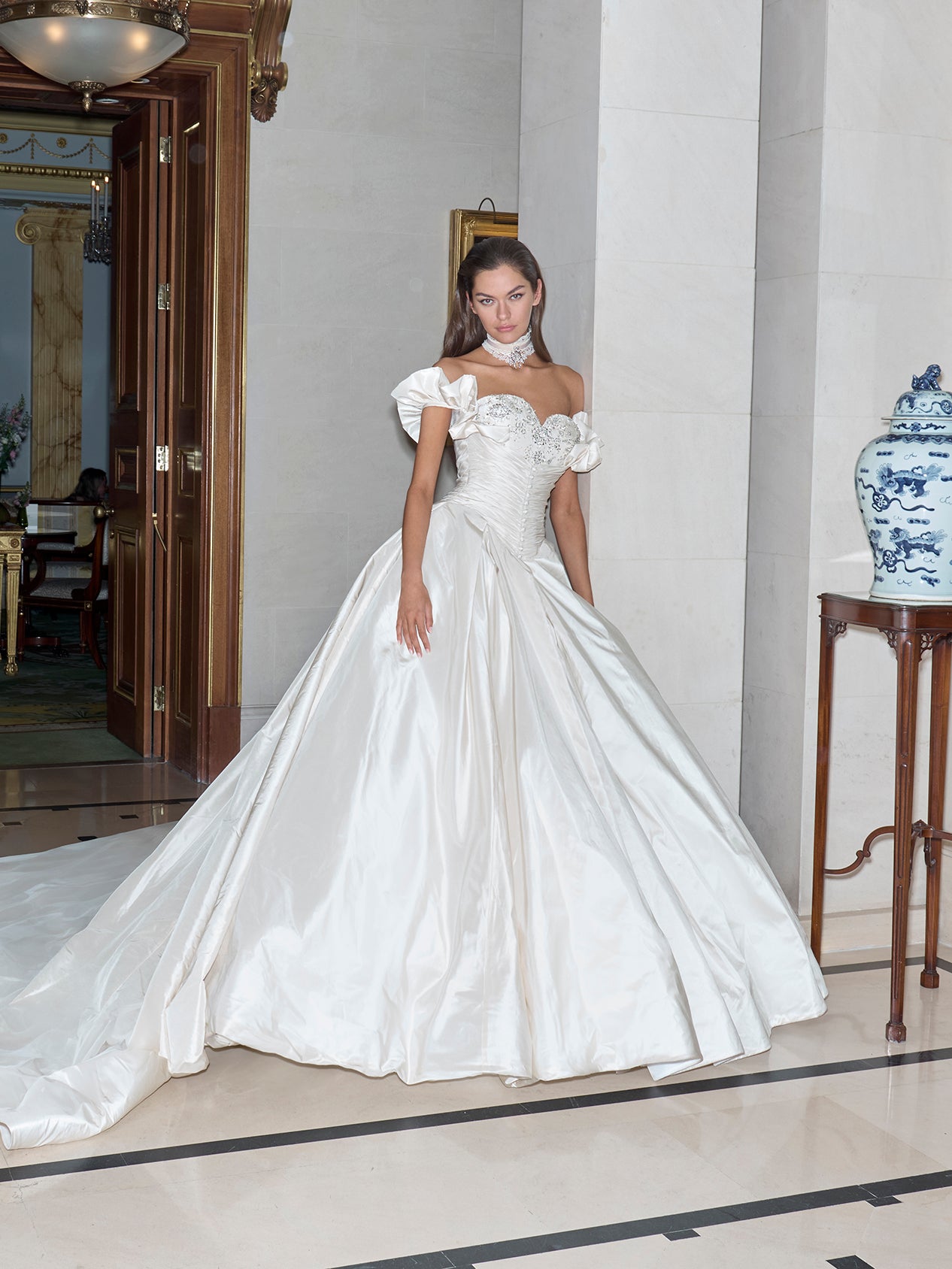 Woman in a white wedding dress standing in an elegant room with classical architecture.