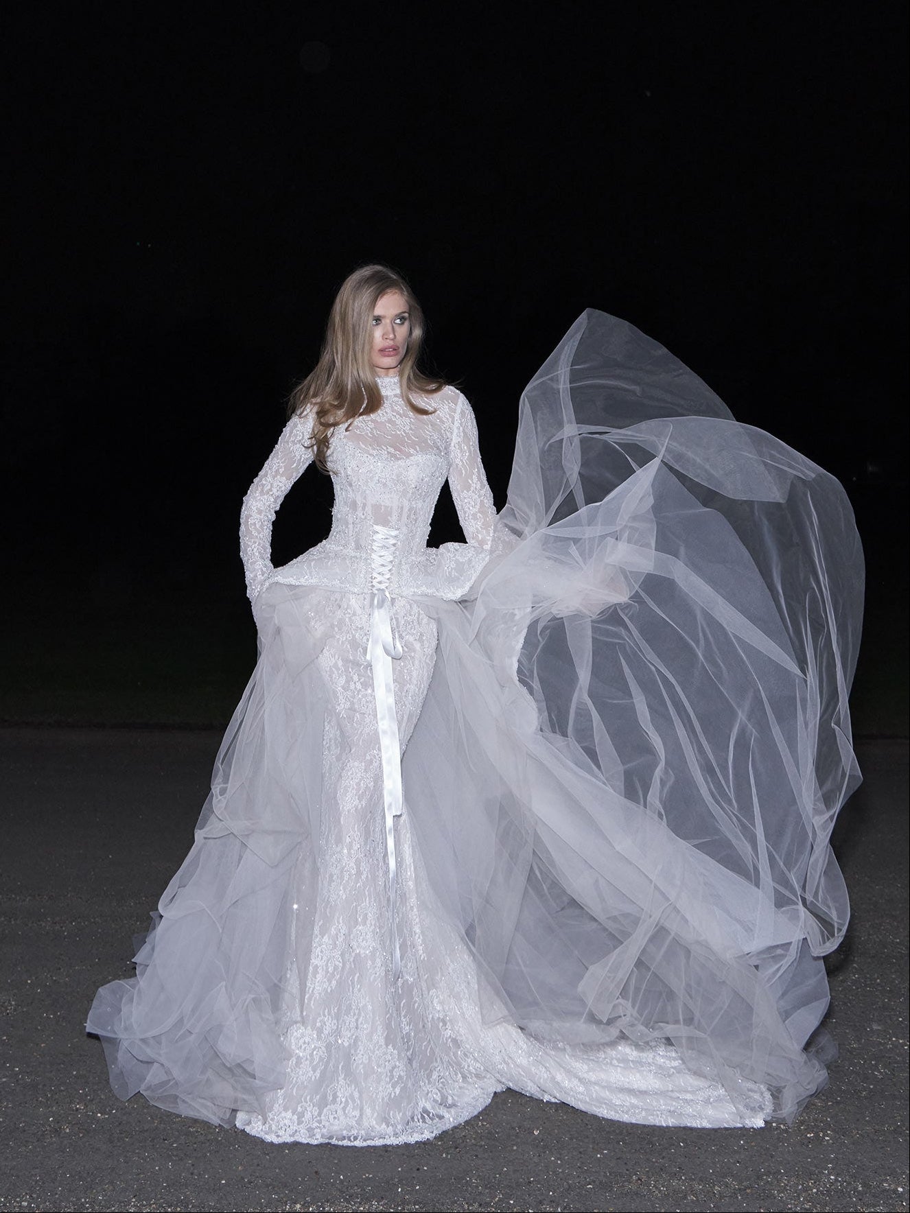 Woman in a white wedding dress with a long train against a dark background