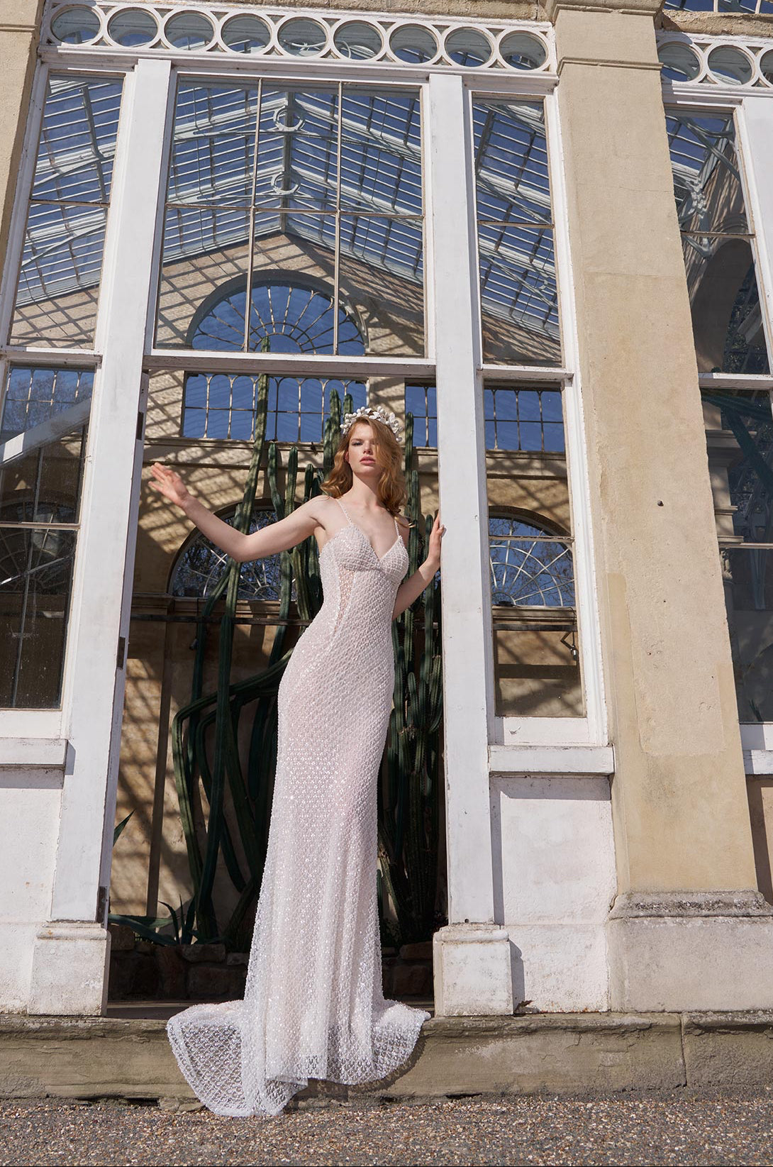 Woman in a white dress standing in front of a large glass conservatory.