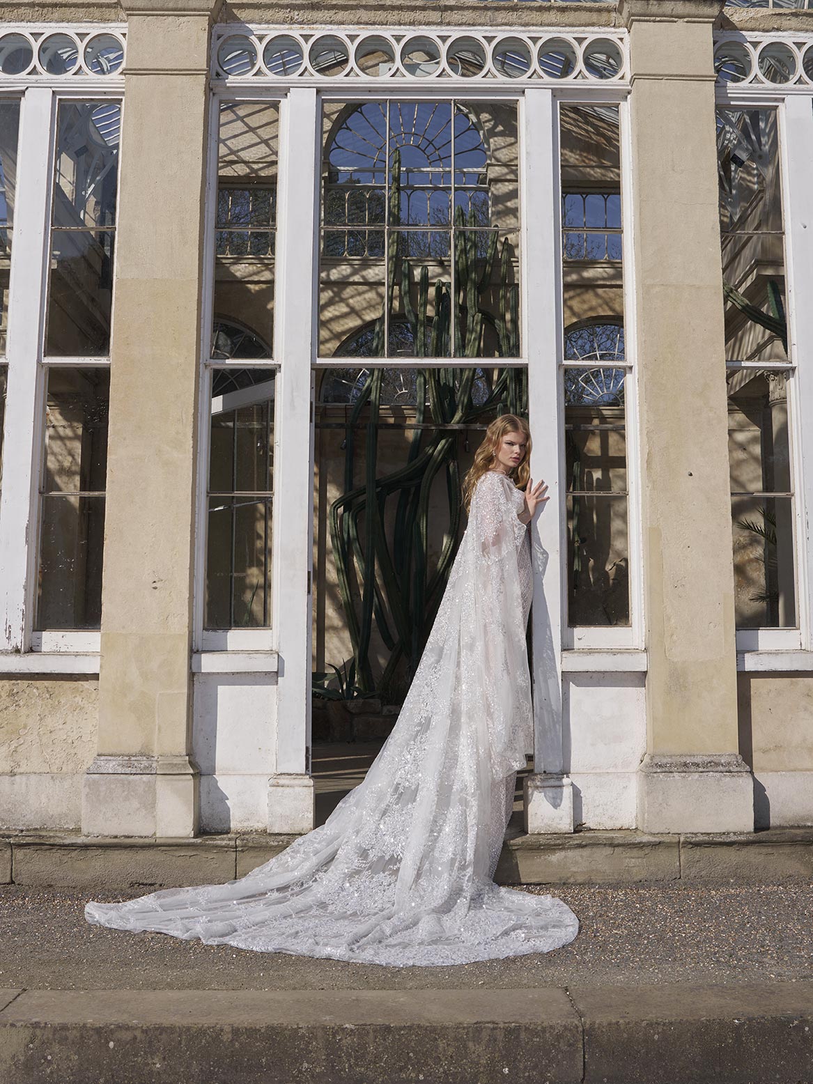 Woman in a long, elegant dress standing in front of large glass windows.