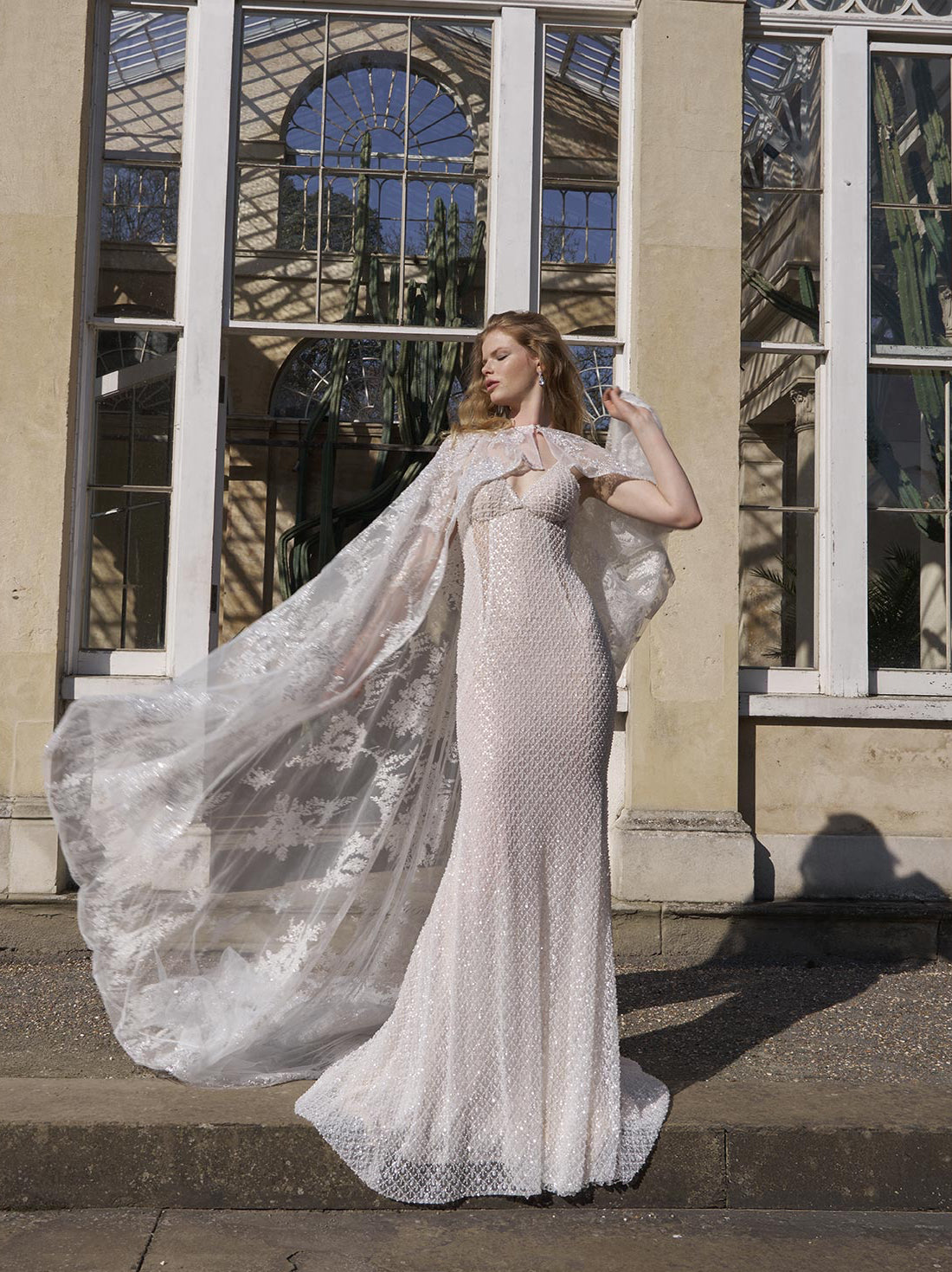 Woman in a white lace gown standing on steps with a large window in the background