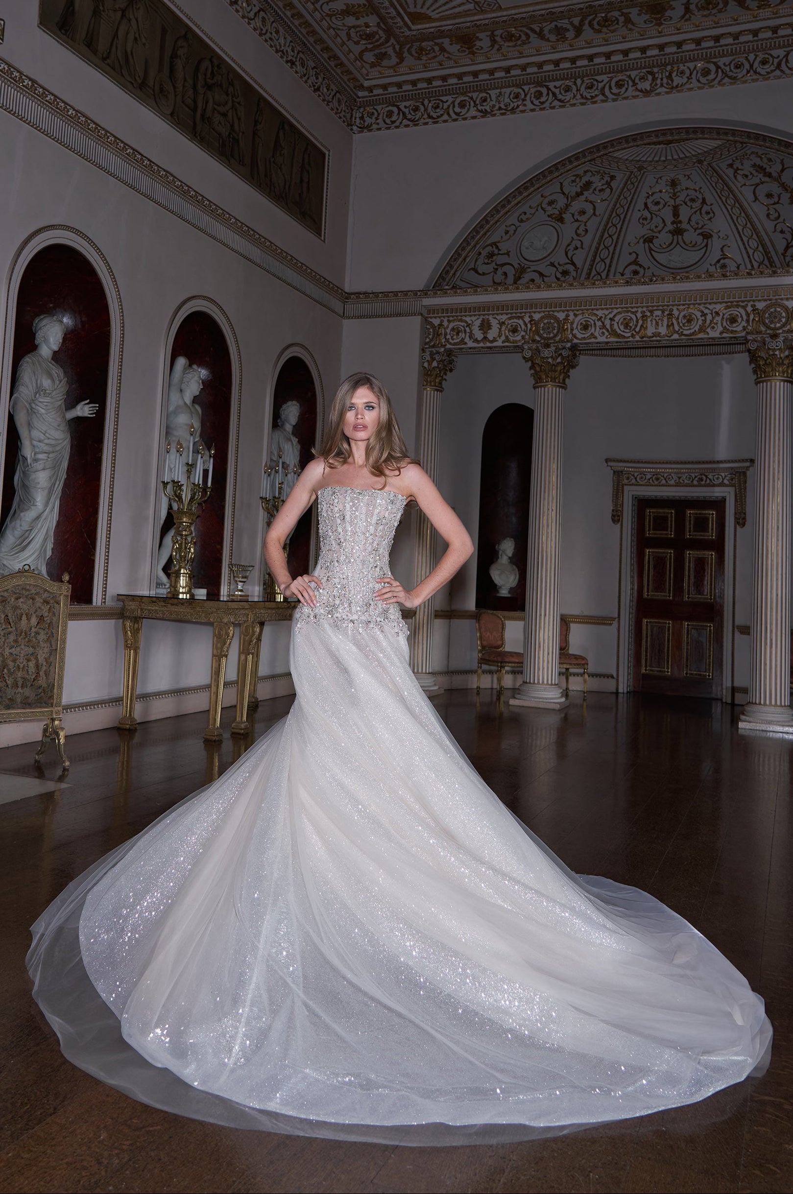 Woman in a white wedding dress standing in an ornate room with classical architecture.