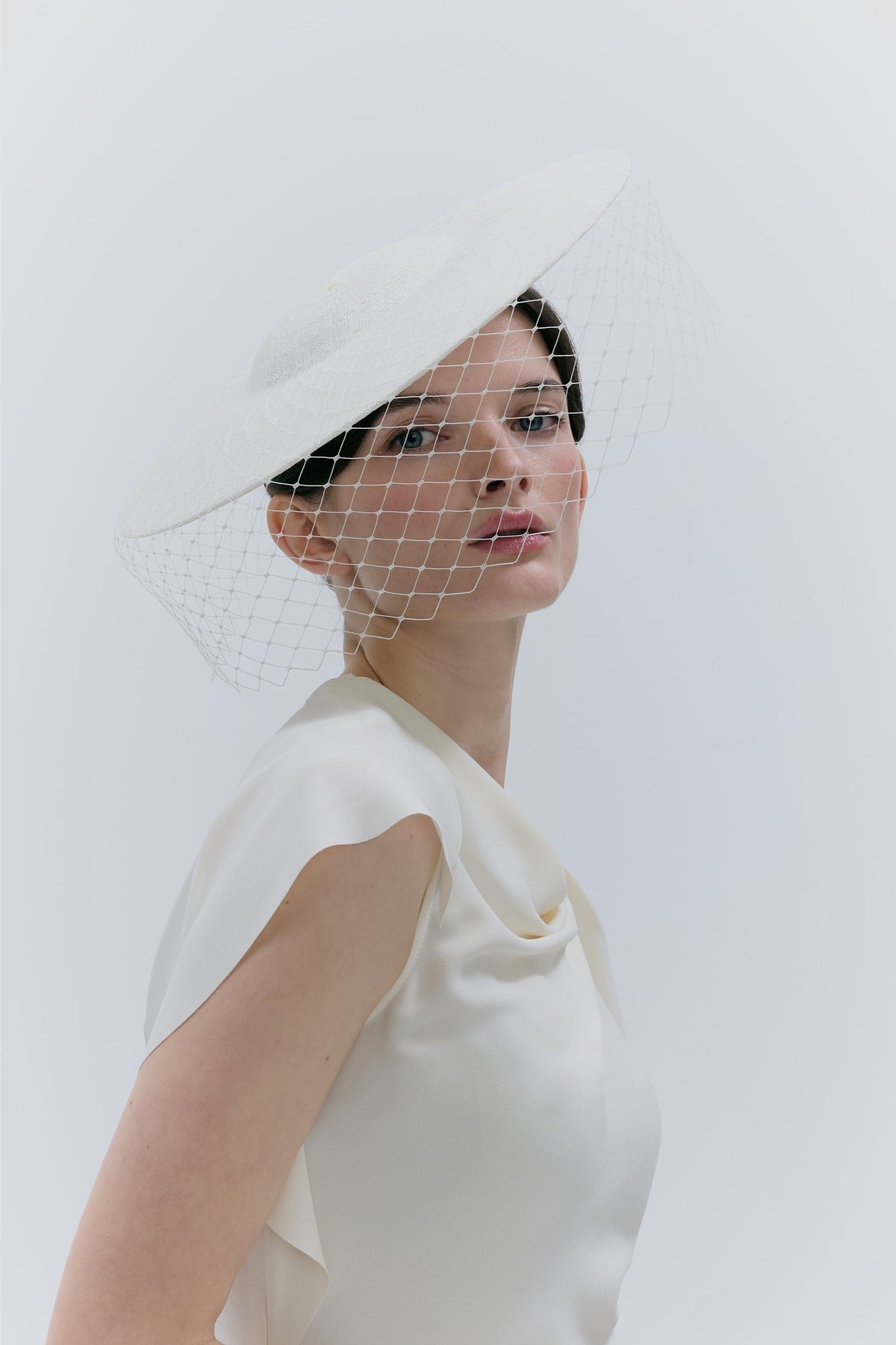 Woman wearing a white bridal veil and dress against a light background