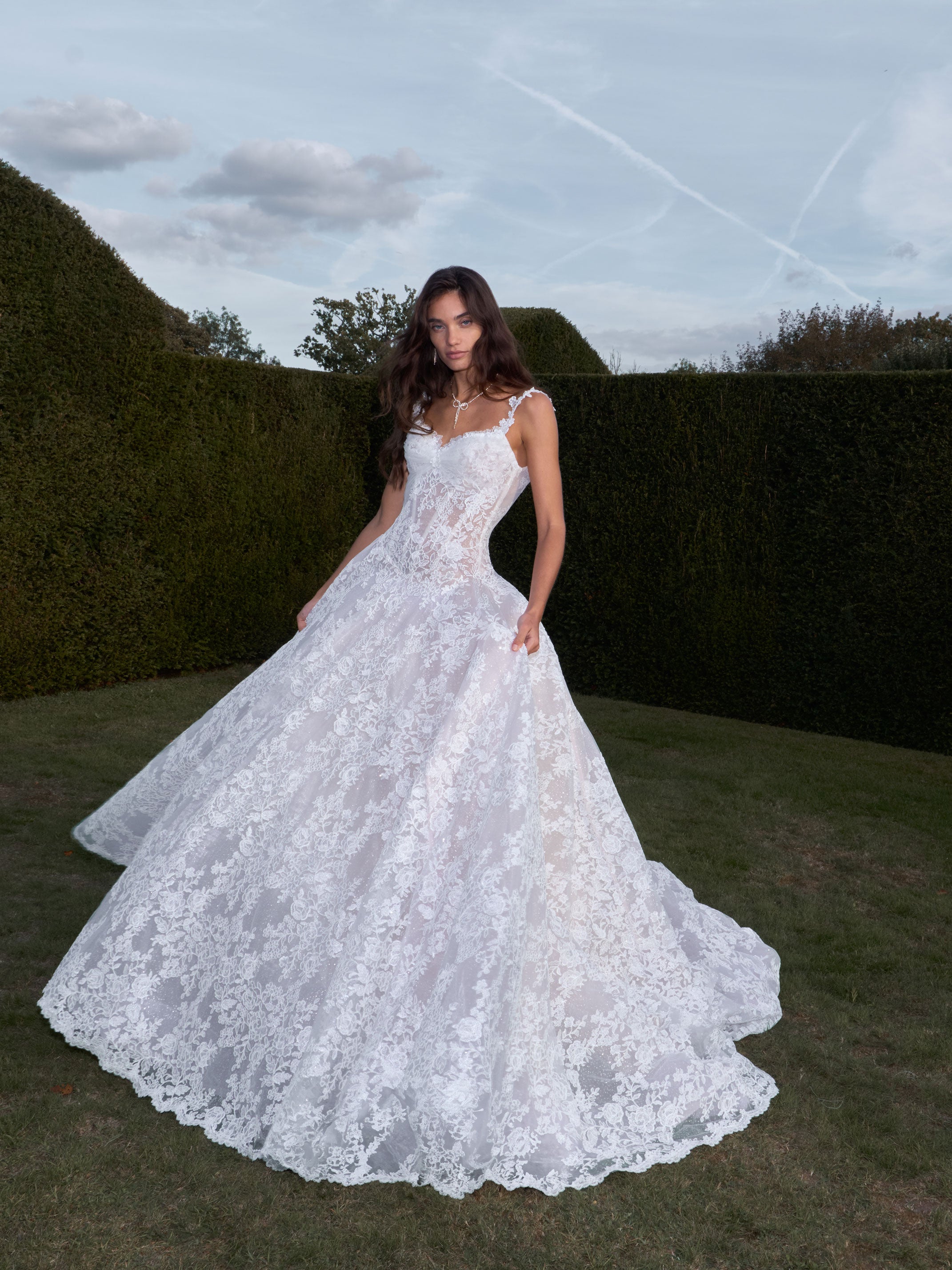 Woman in a white lace wedding dress standing outdoors with greenery in the background