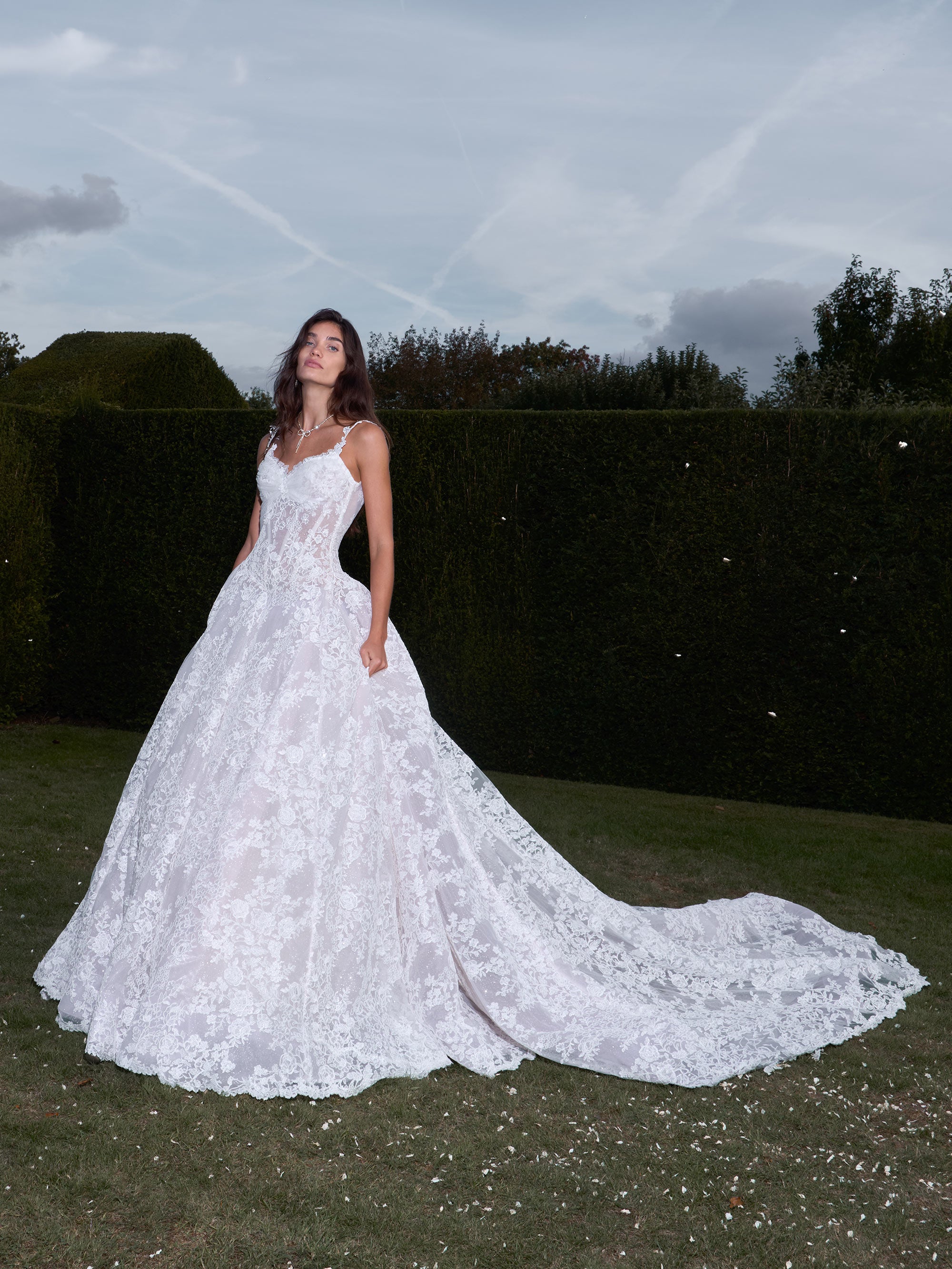 Woman in a white wedding dress standing outdoors with greenery in the background