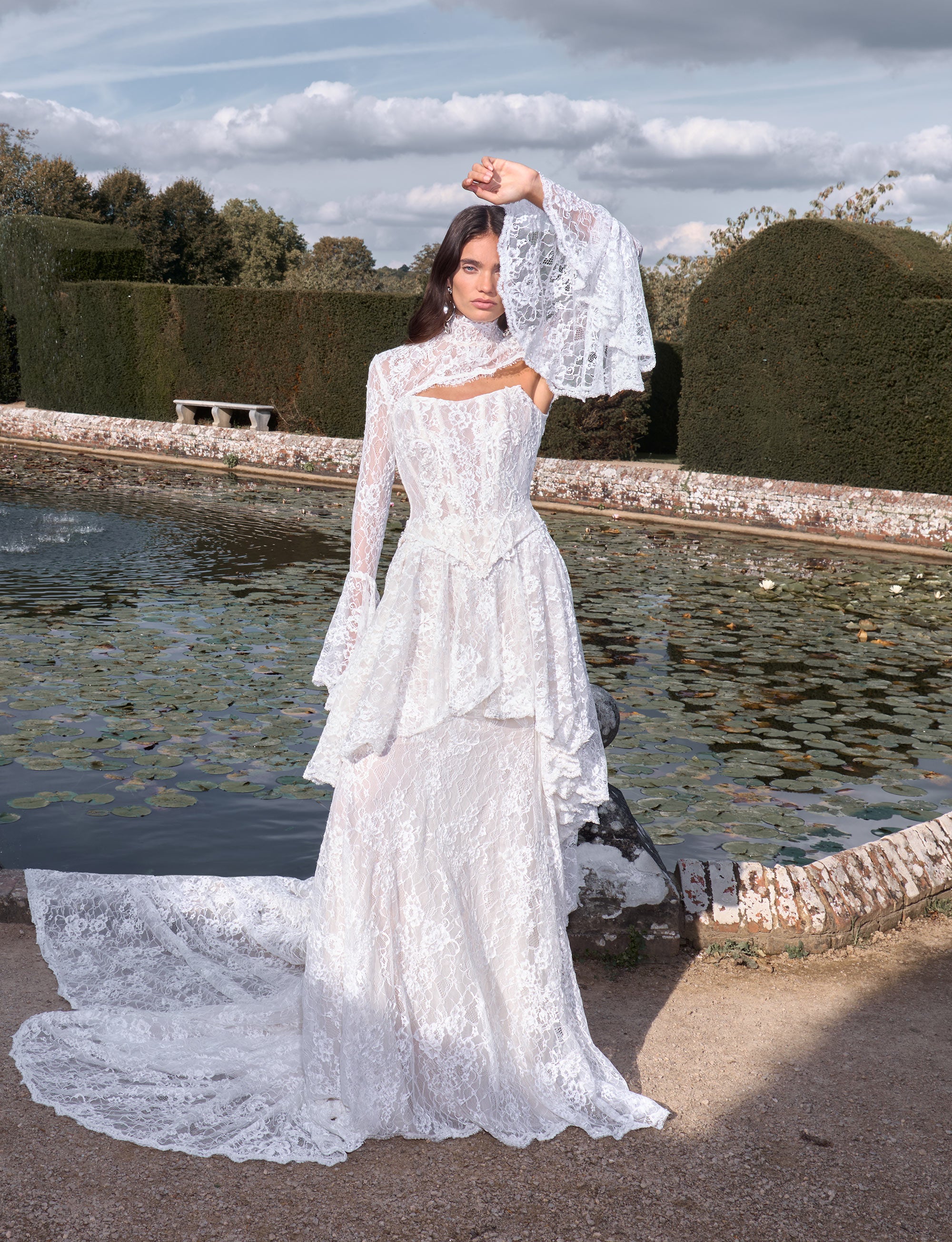Woman in a white lace dress standing by a fountain with a scenic background
