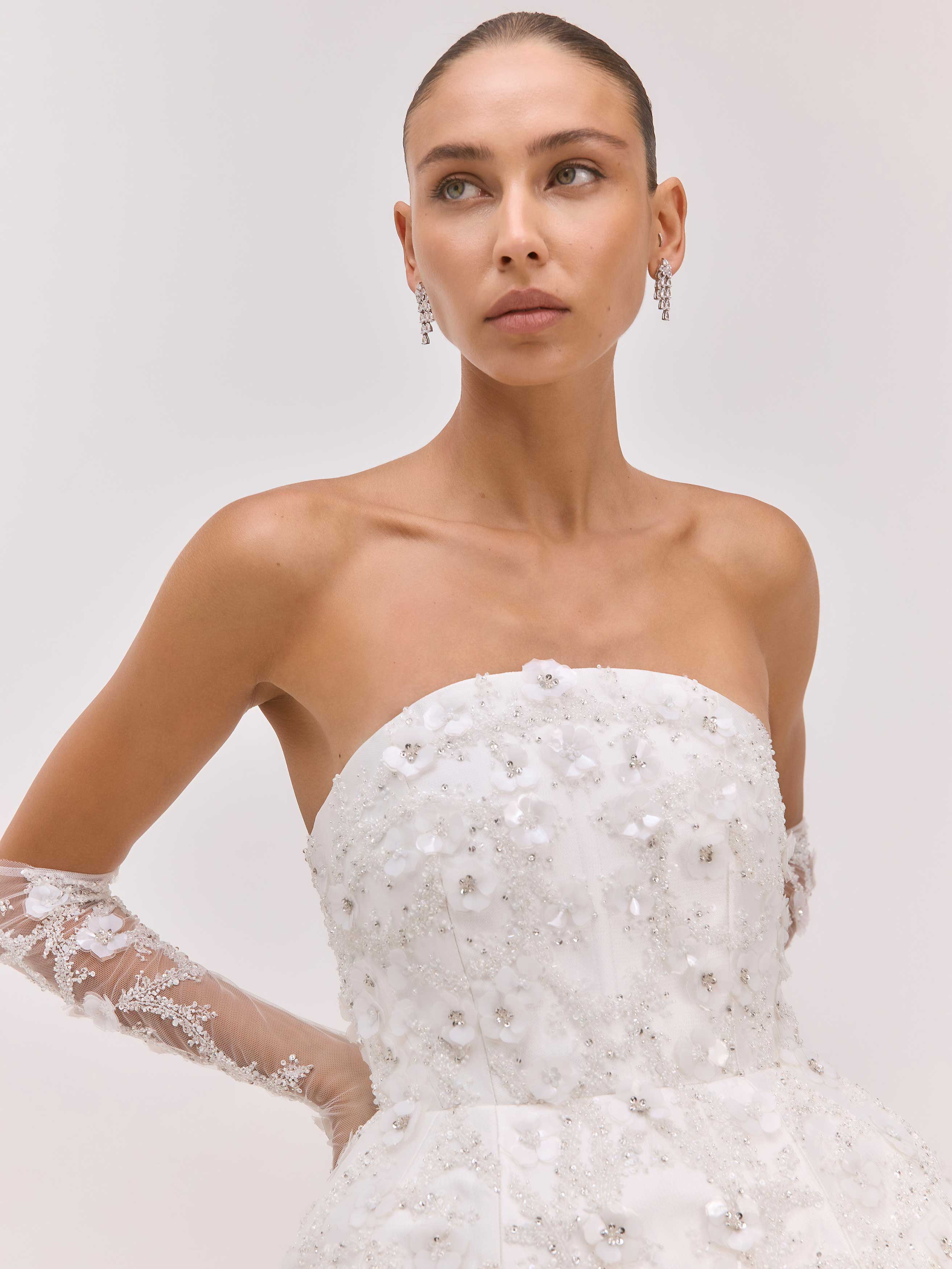 Woman wearing a strapless, beaded wedding dress against a plain background