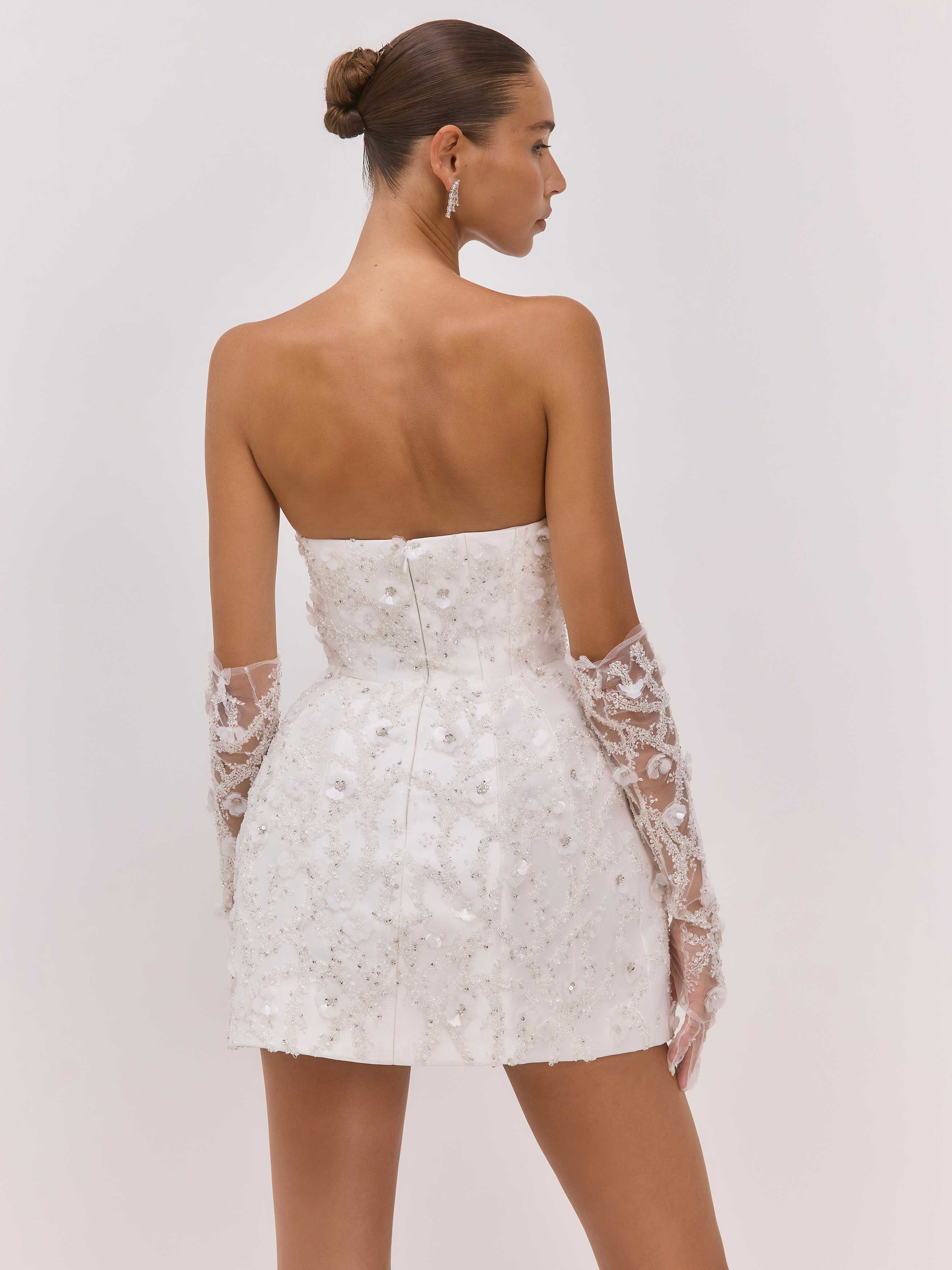 Woman wearing a white strapless dress with lace sleeves on a plain background