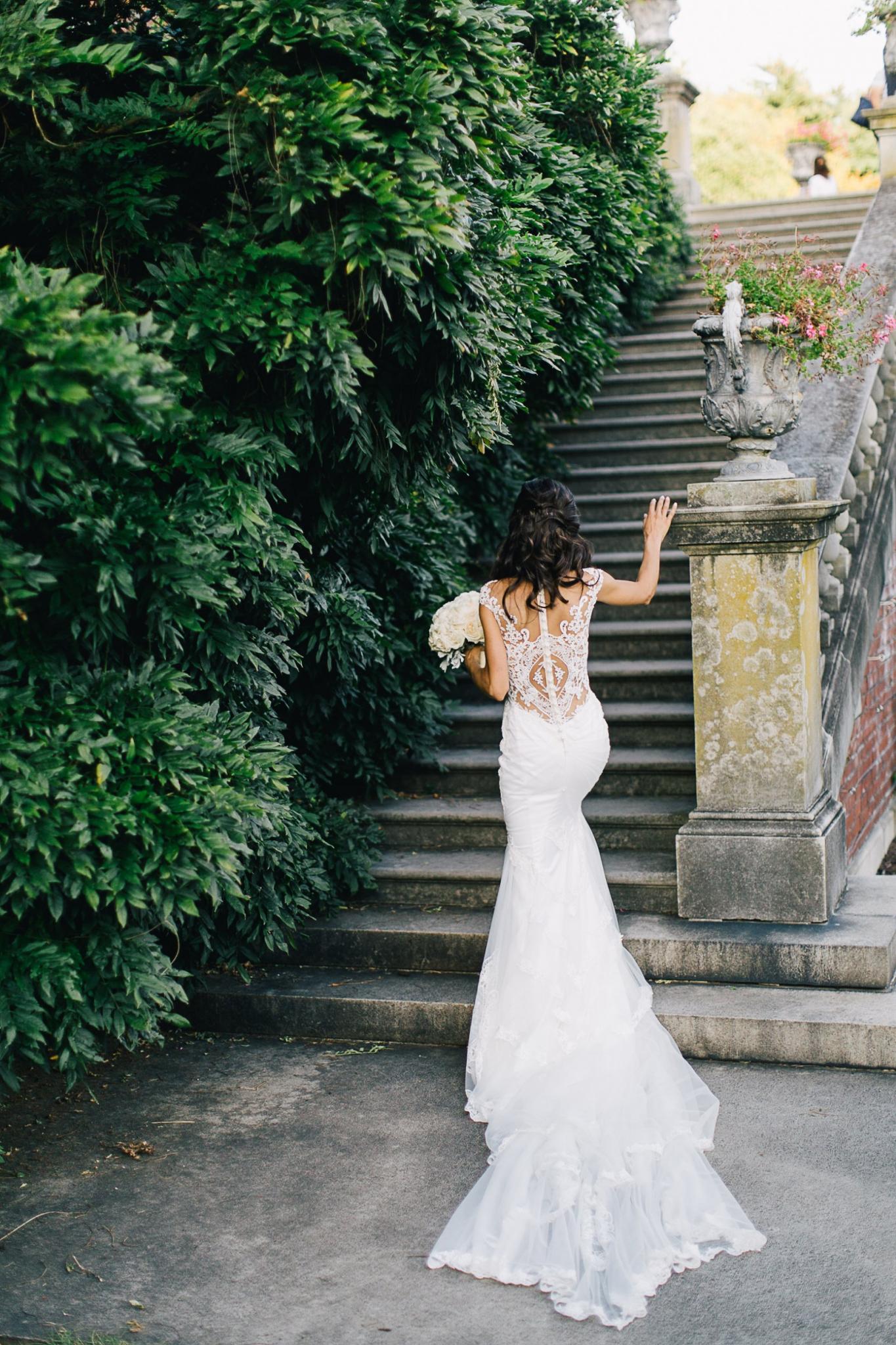 GL Bride Jennifer in our Fiona gown outside next to ornate stairs and greenery