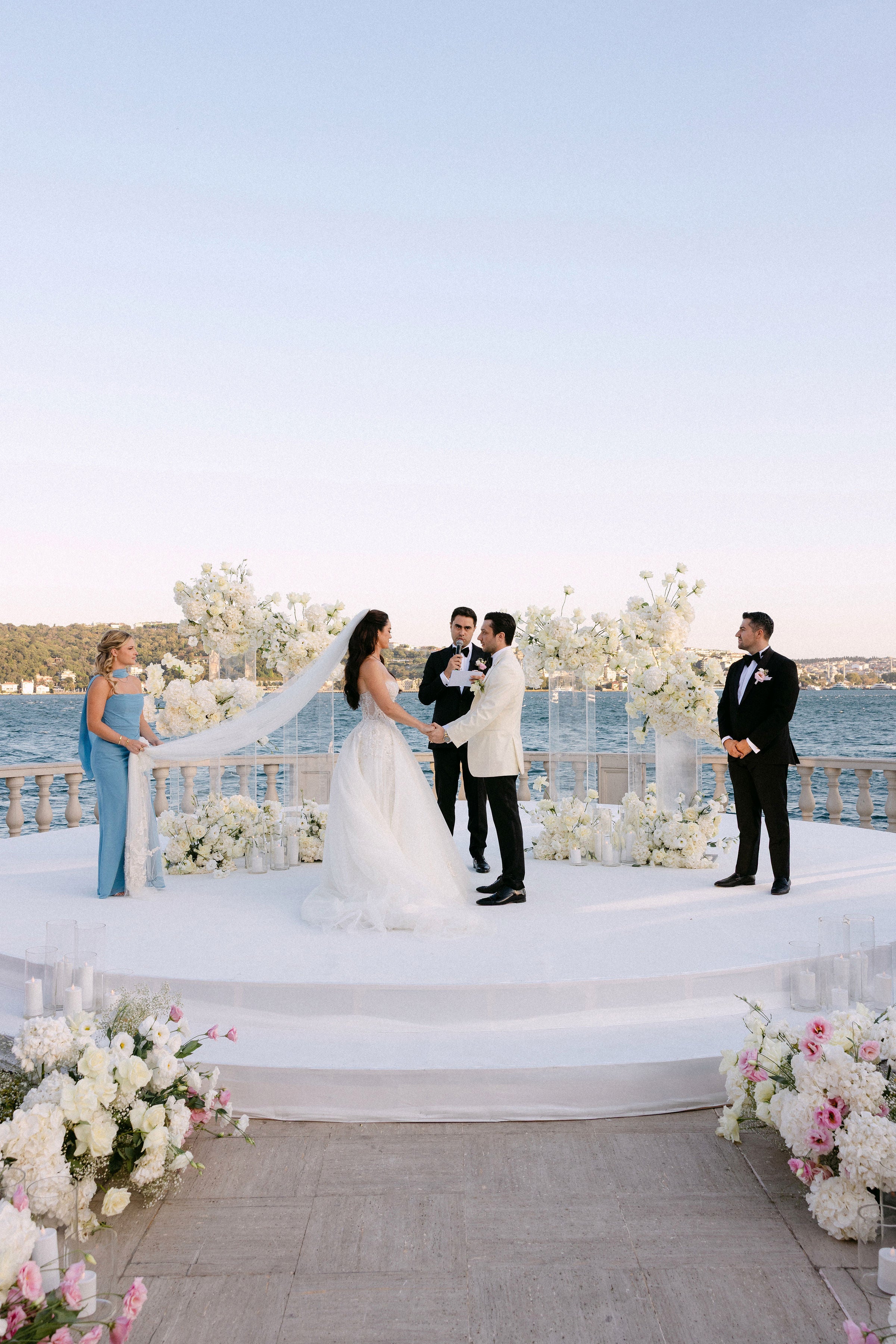 Wedding ceremony by a waterfront with floral decorations and guests.