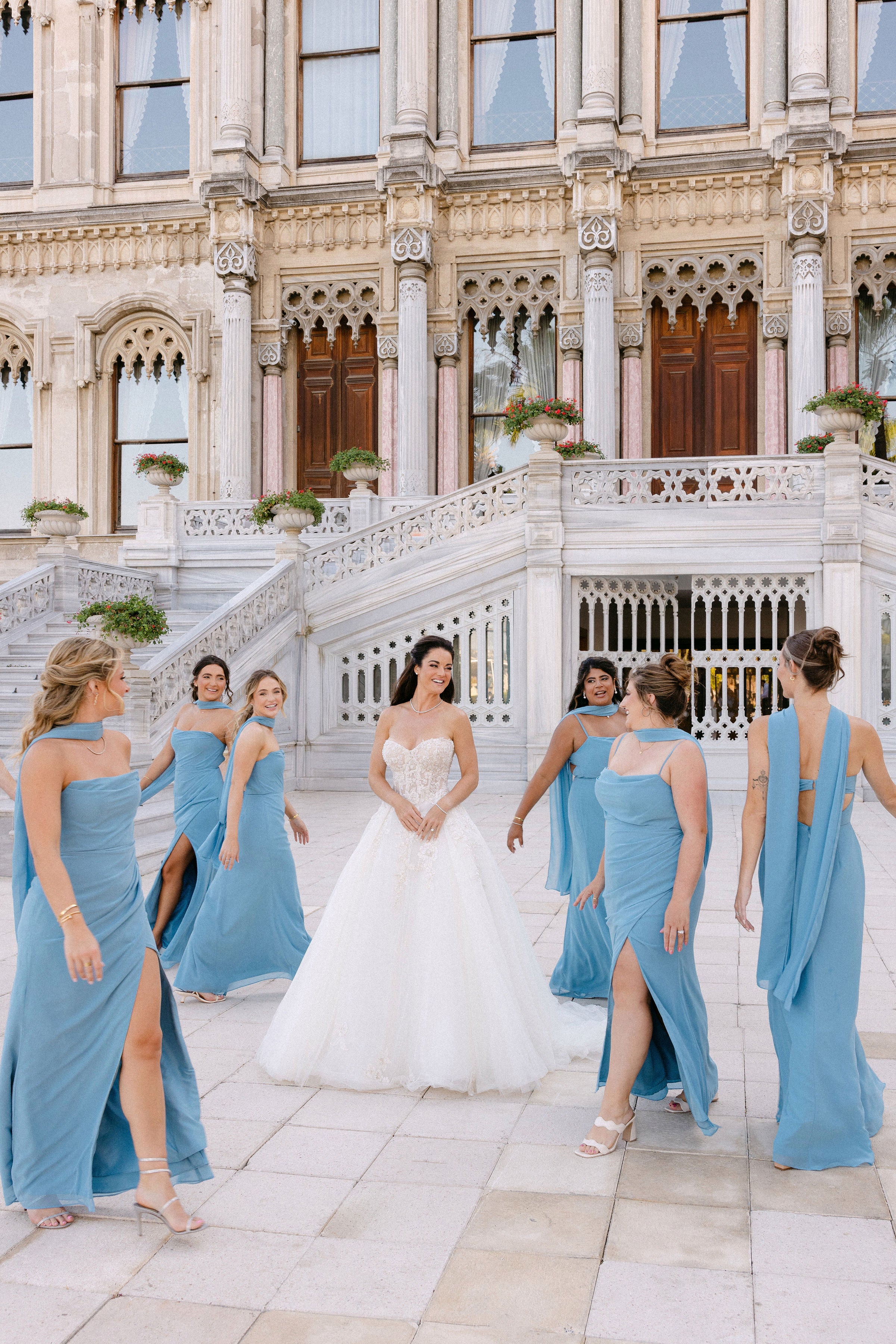 Bride with bridesmaids in blue dresses in front of an elegant building.