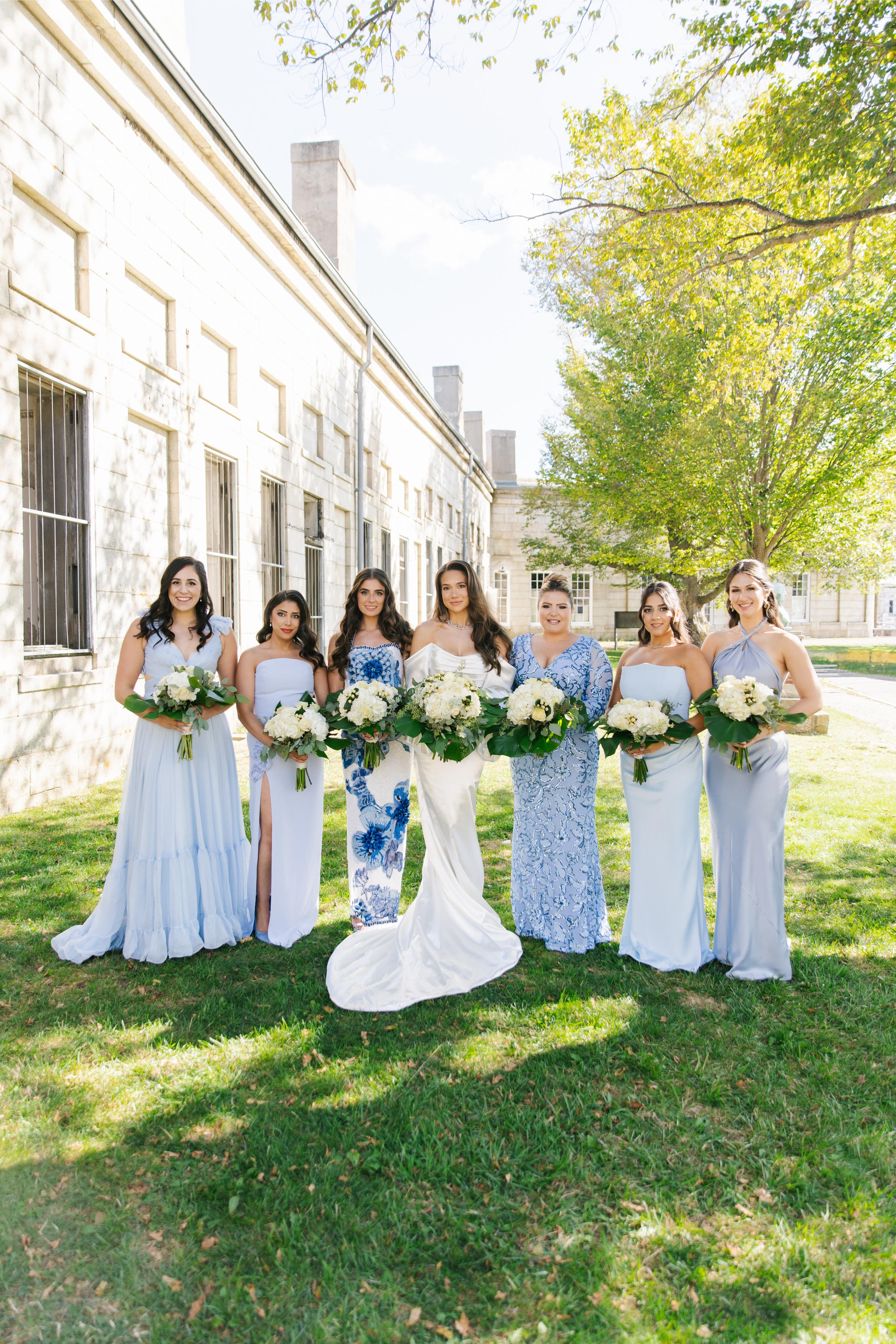 GL Bride Alexandra in Galia Lahav's Alona  and her bridesmaids with floral bouquets standing in front of a building.