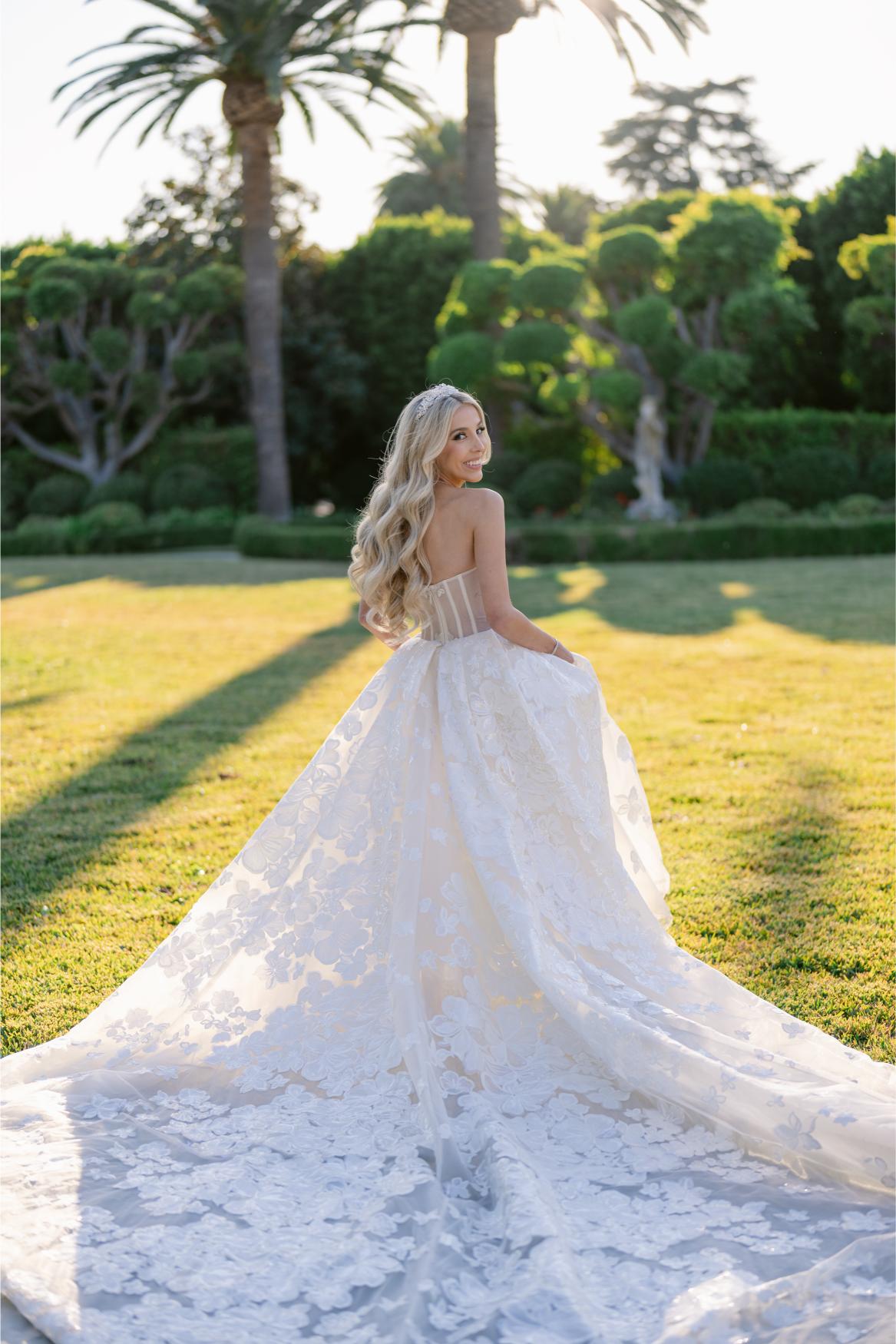 GL Bride Anaies in the Renee wedding dress from Galia Lahav's Rise Collection standing in a garden with palm trees.