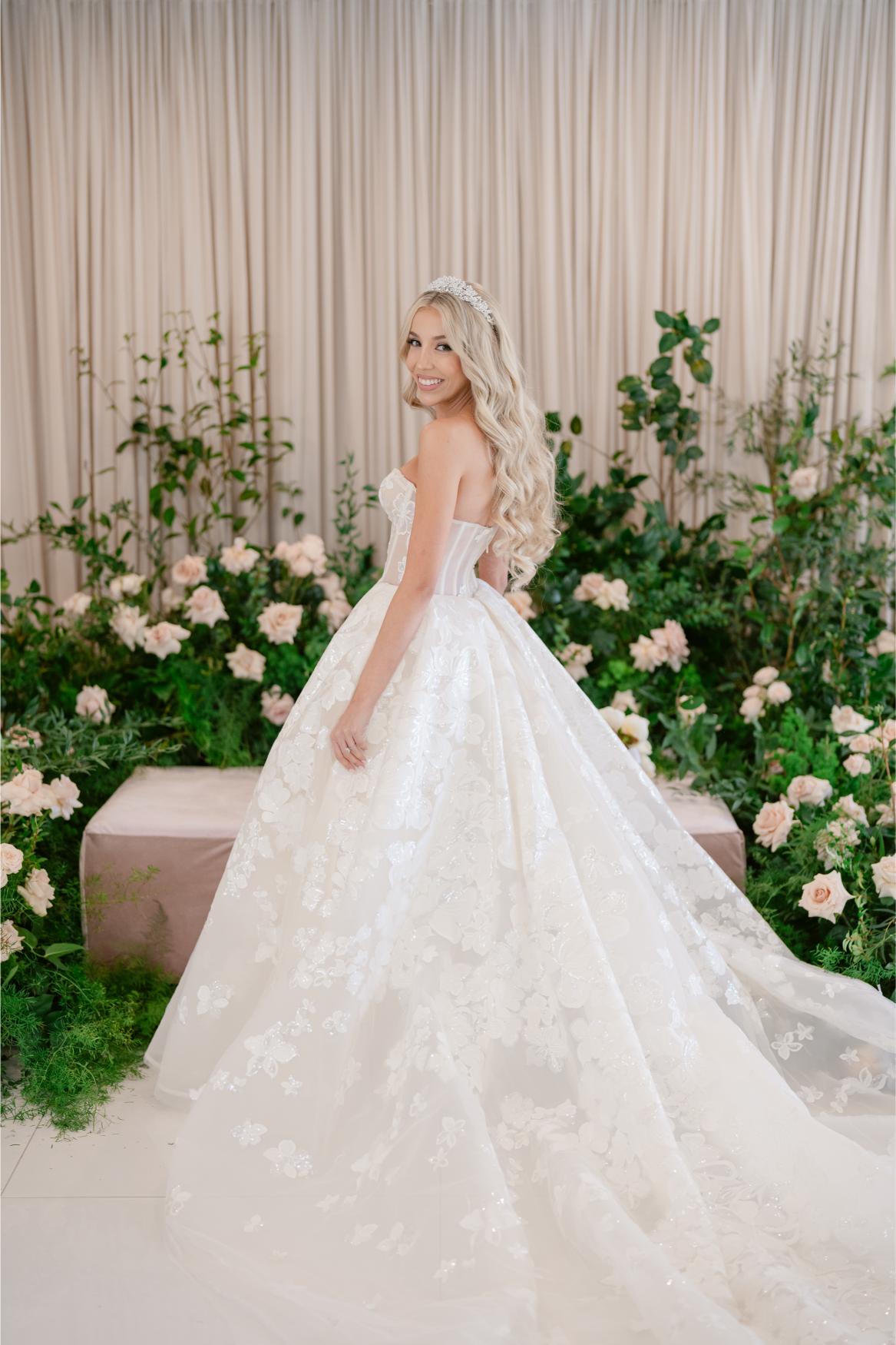GL Bride Anaies in the Renee wedding dress by Galia Lahav standing among flowers and greenery.