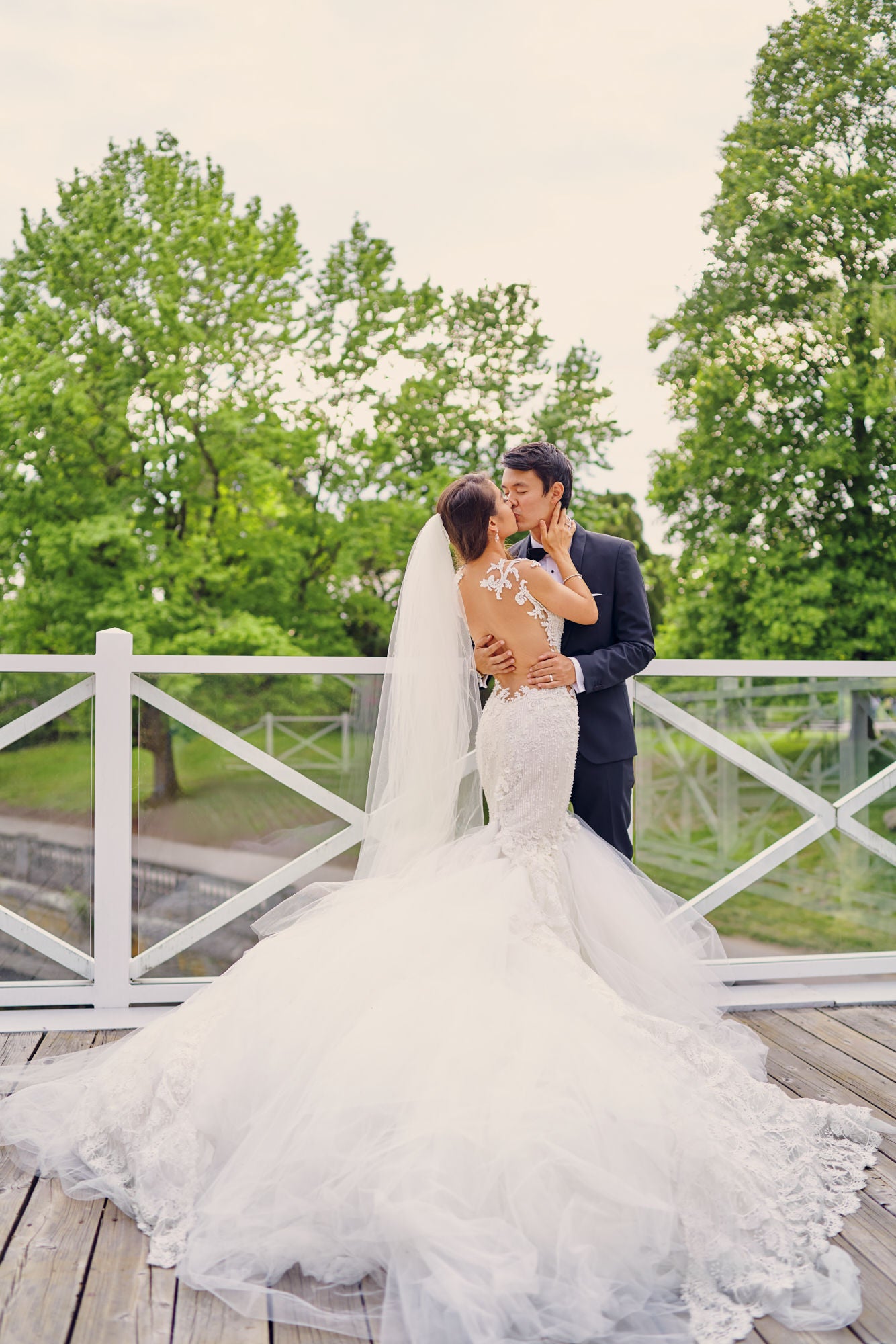GL Bride Anita wearing our Ms. Elle kissing her groom on a scenic bridge 