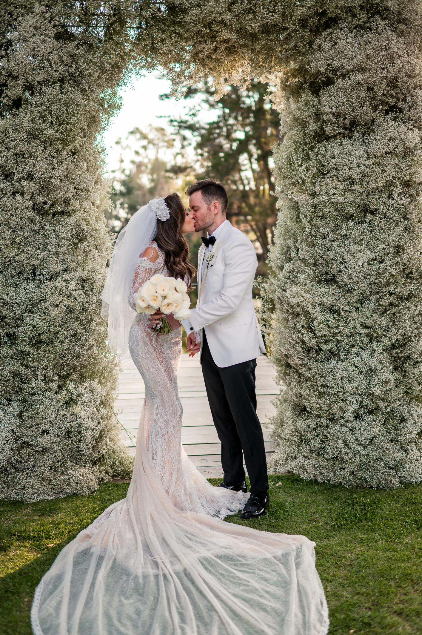 GL Bride Betty Luna in our Élysée,  in an floral arch way, embracing her husband 