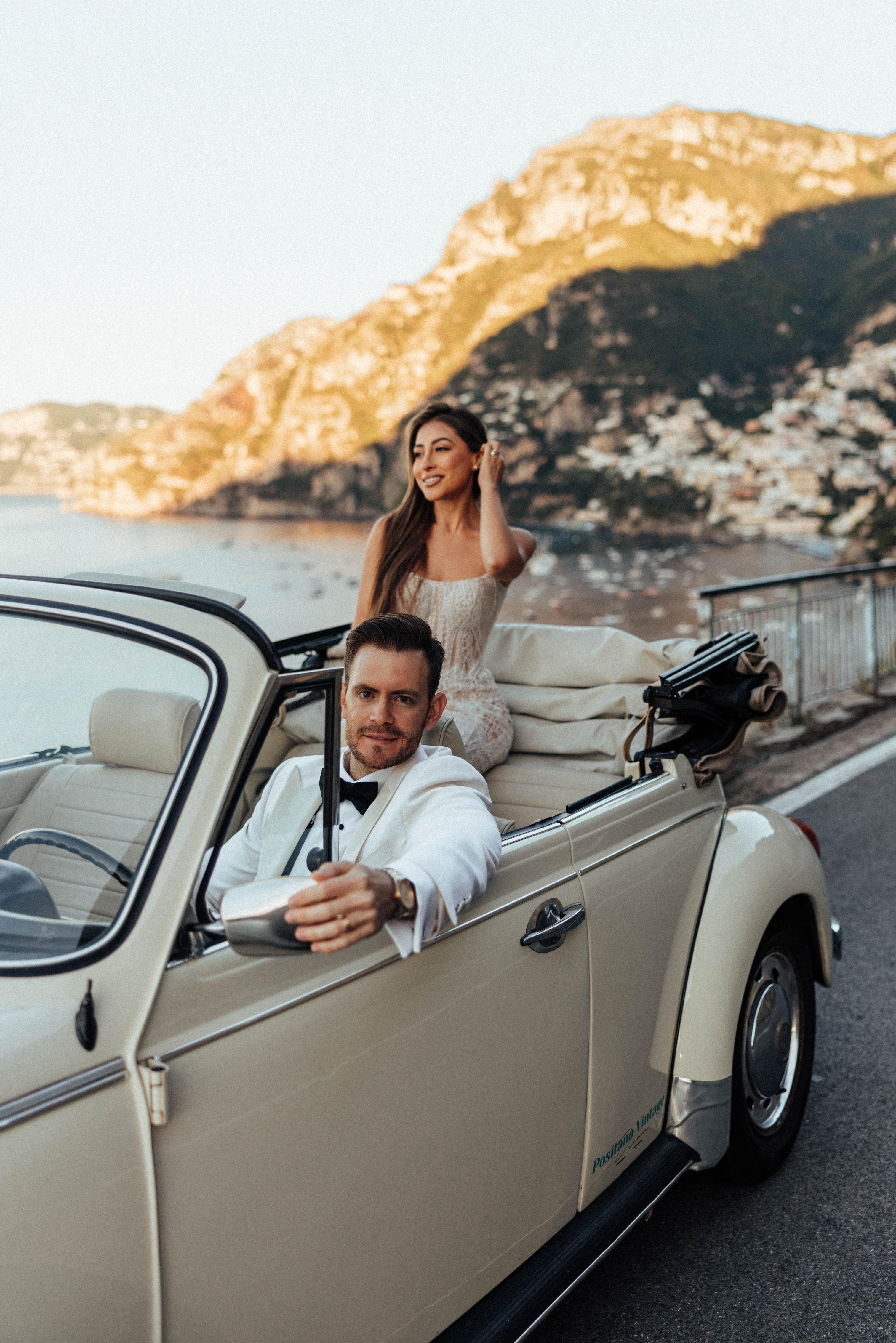 GL Bride Betty Luna in our Élysée in the vintage car with her husband driving, near an oceanside 