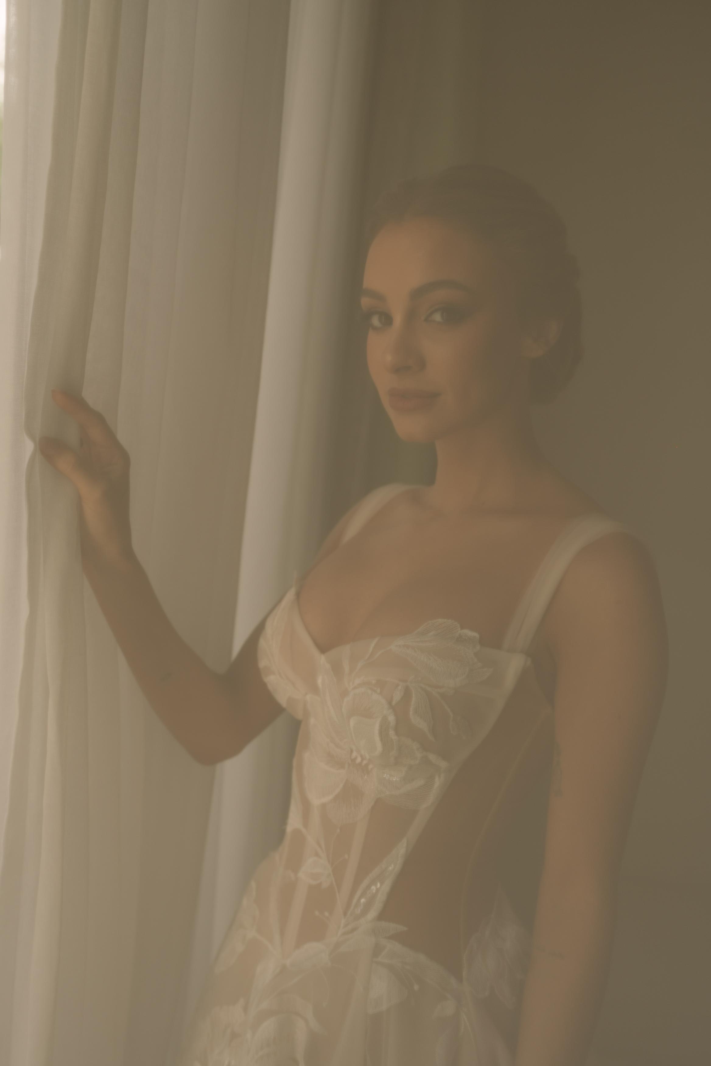 Woman in a light dress standing behind a curtain in a softly lit room